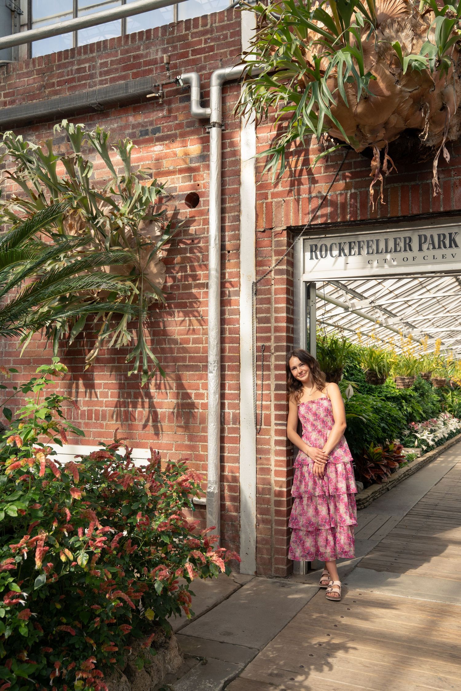 Pink floral dress photographed along brick walkway at Rockefeller Park with senior in lush greenery.