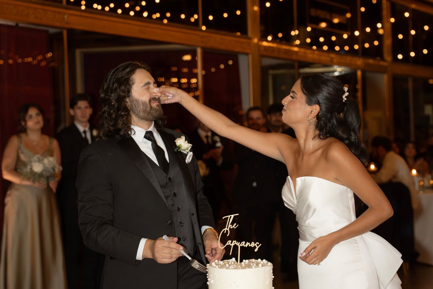 A bride and groom share their first dance at a wedding reception under warm string lights.