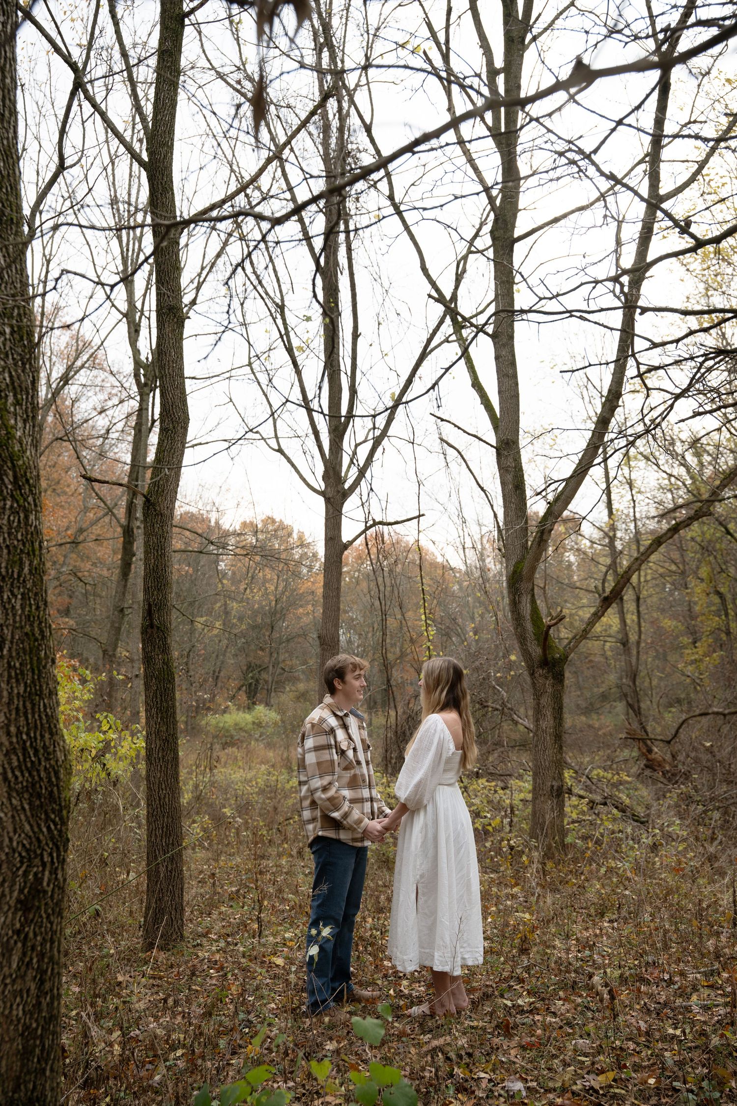 Couple walking through bare winter trees in a wooded area.