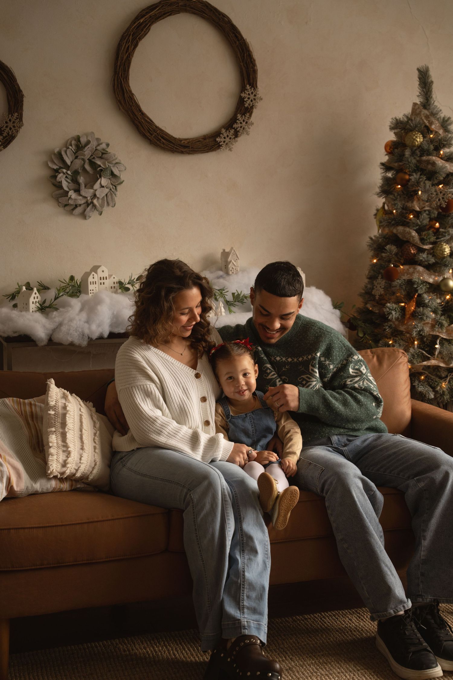 A family shares a tender moment on a brown studio couch with Christmas decorations in the background.