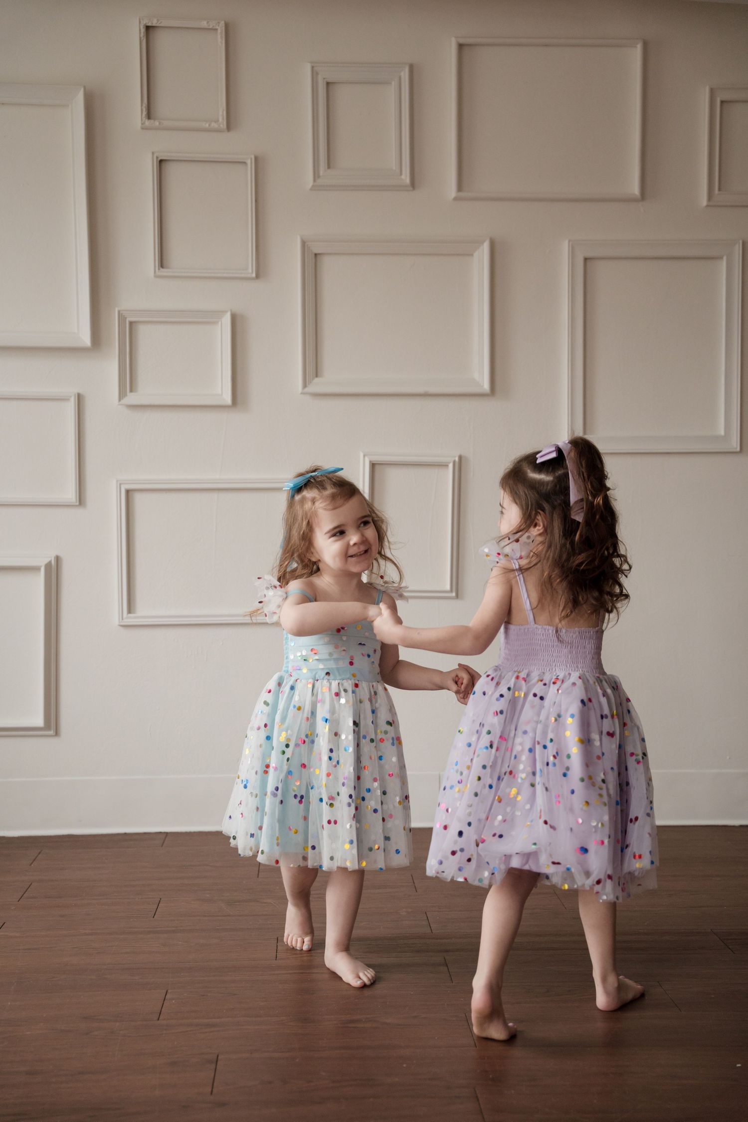Two children in floral dresses dancing together on studio hardwood floor.