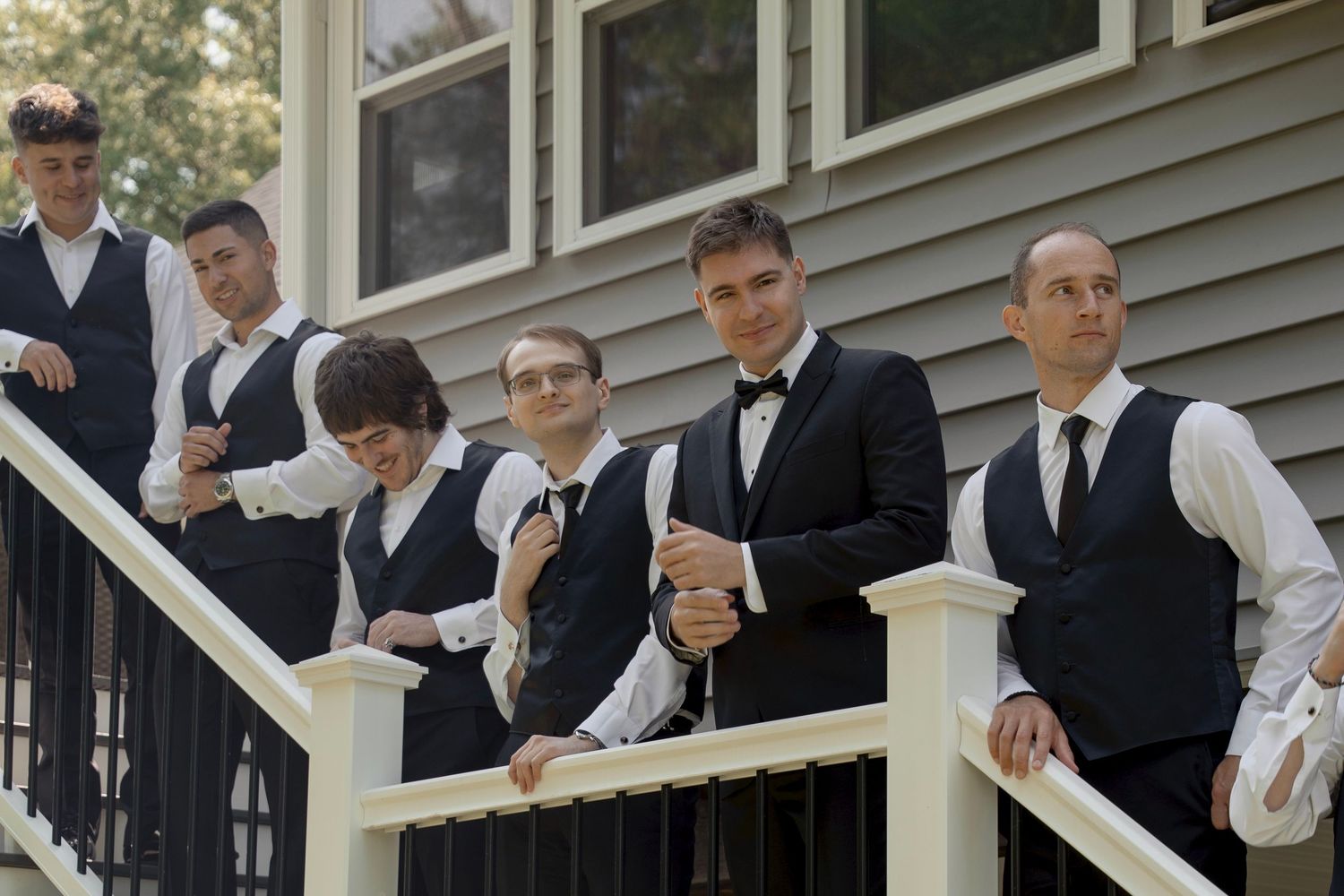 Groomsmen in formal attire pose together on outdoor porch.