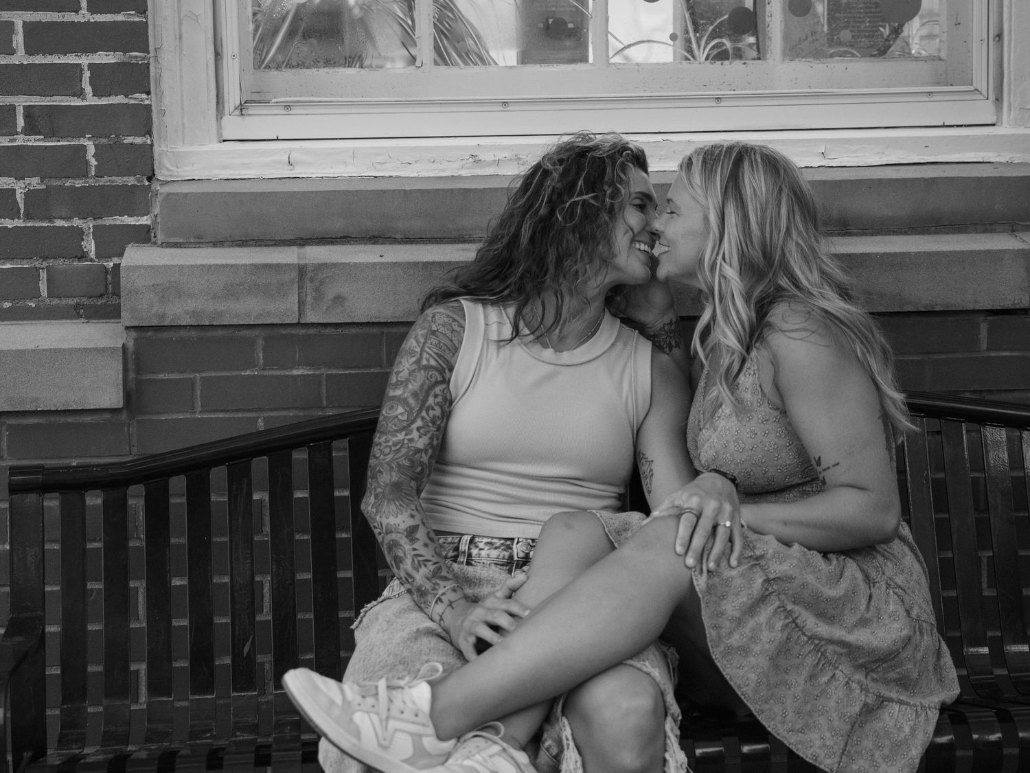 Couple sharing an intimate moment on a bench by a brick wall.