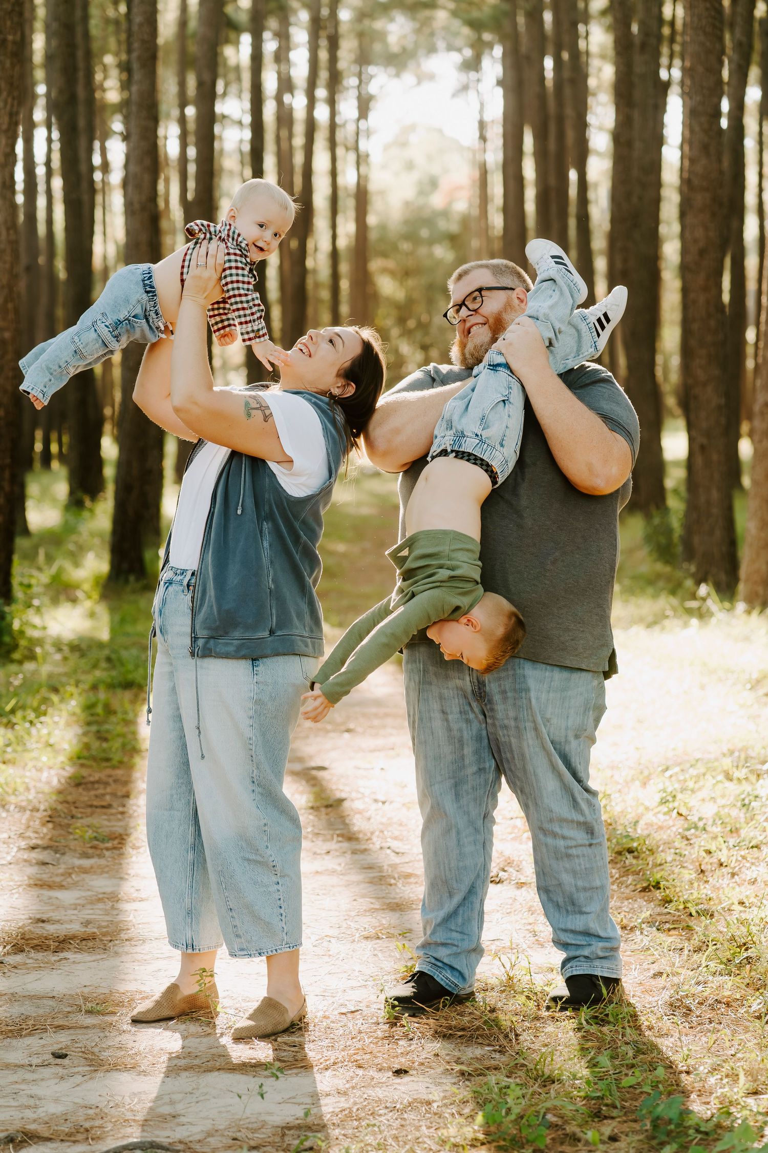 Playful family photos in a sunlit forest path wearing coordinated denim outfits.