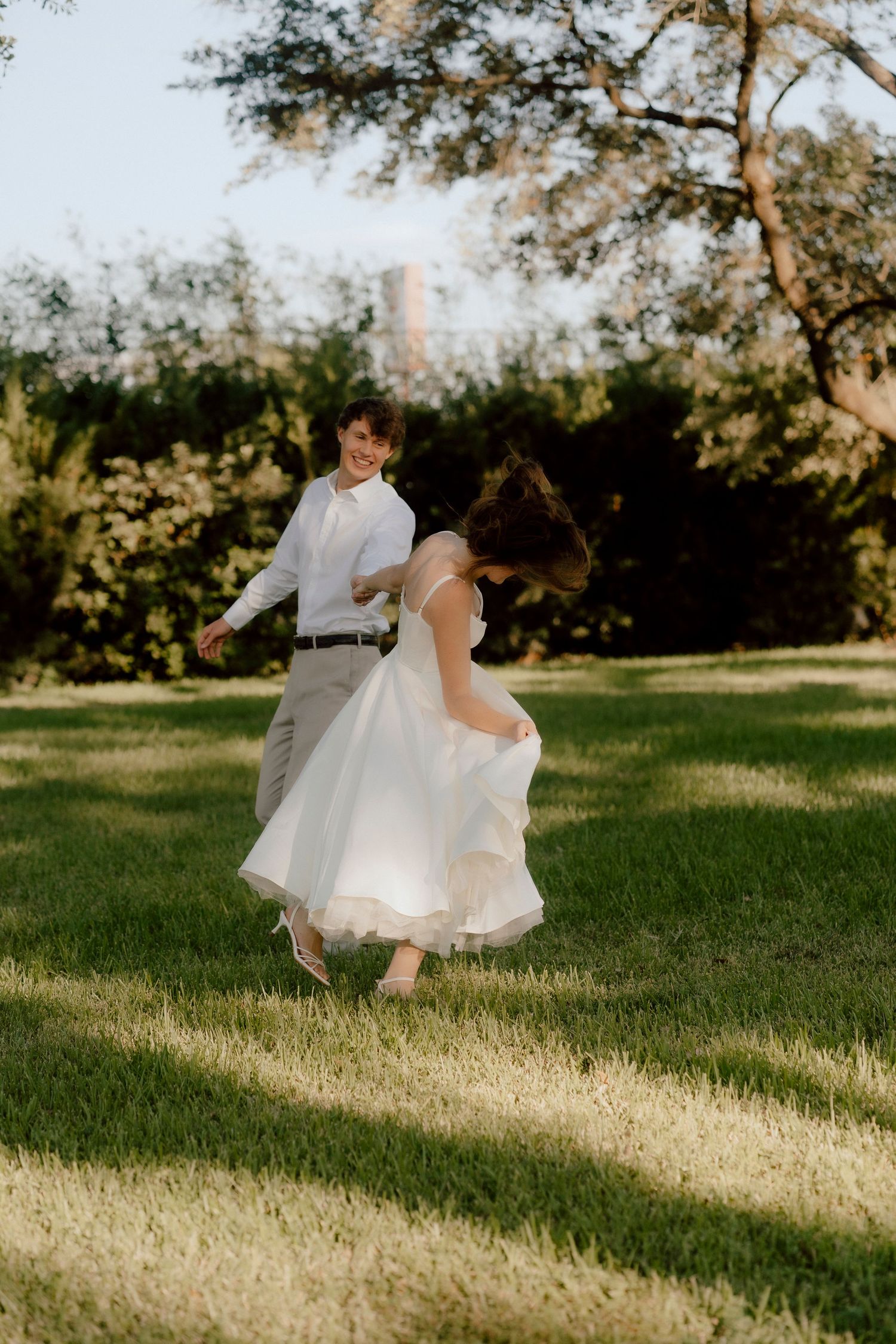 A white wedding dress flows gracefully across a sunlit grassy field during a romantic outdoor photoshoot.
