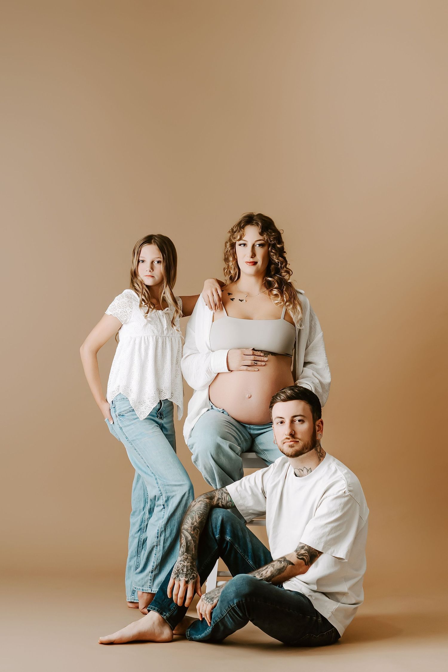 Artistic maternity studio portrait with neutral beige background and casual styling.