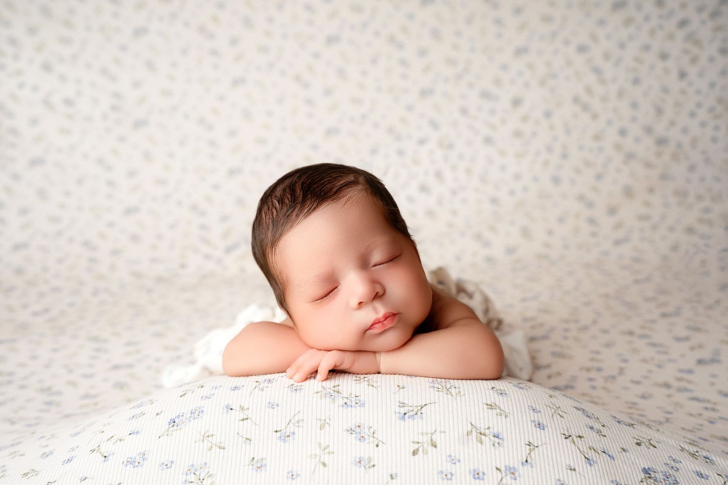Peaceful newborn baby sleeping on a floral blanket with hands tucked under chin.