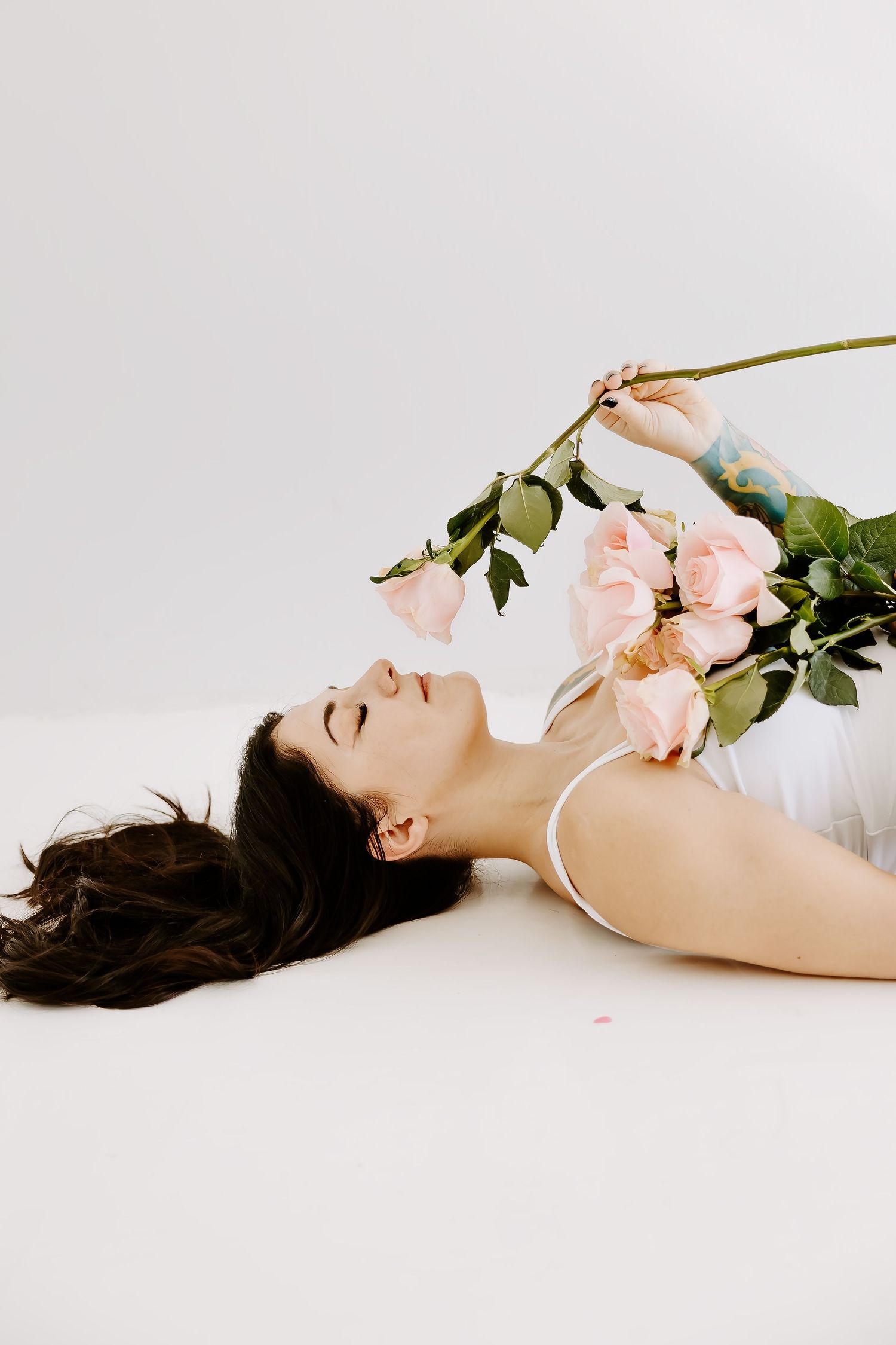 Minimalist boudoir photography with pink roses on white background.