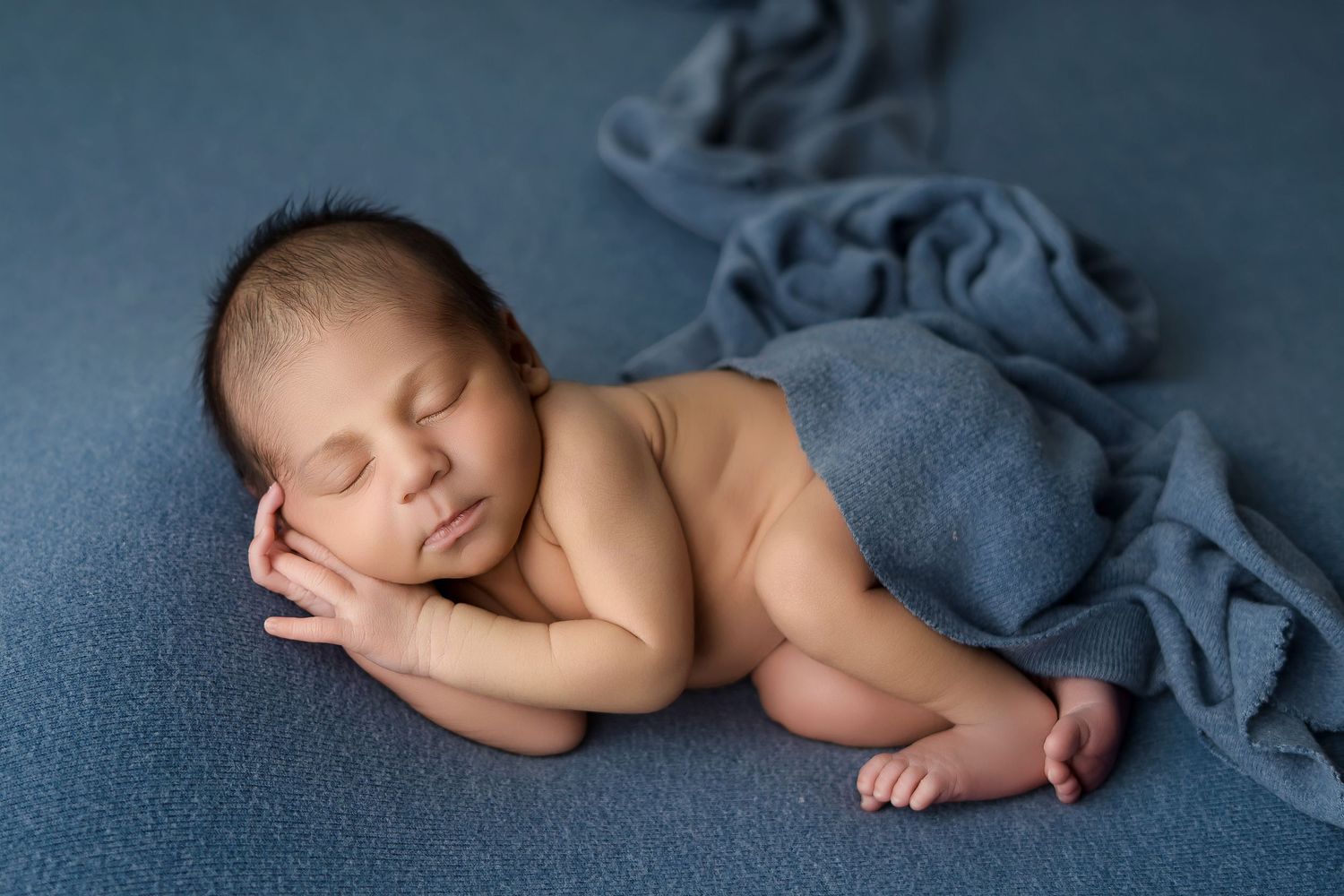 Peaceful newborn baby sleeping curled up on a soft blue blanket with bare feet visible.