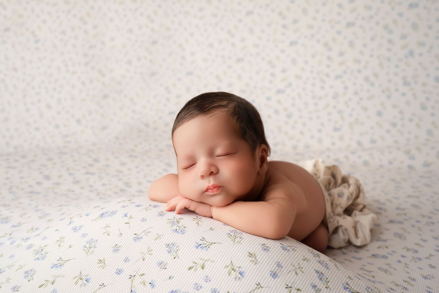 Peaceful newborn baby sleeping on a floral blanket with hands folded under chin in a professional portrait.