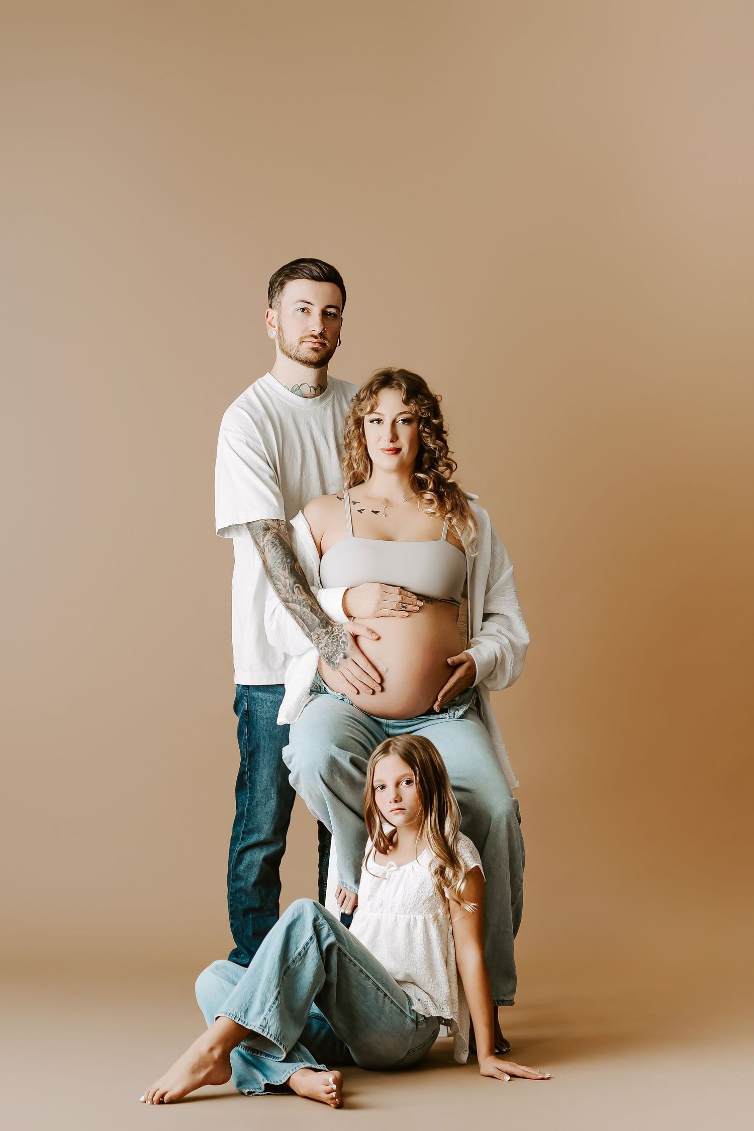 Casual family maternity portrait against neutral beige background in studio setting.