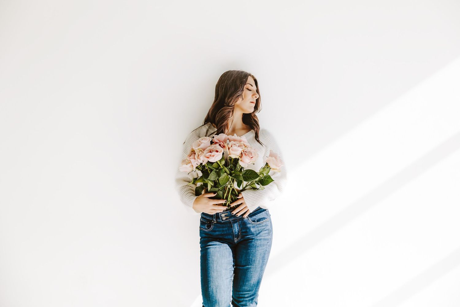 Artistic portrait series with woman holding flowers against white wall.