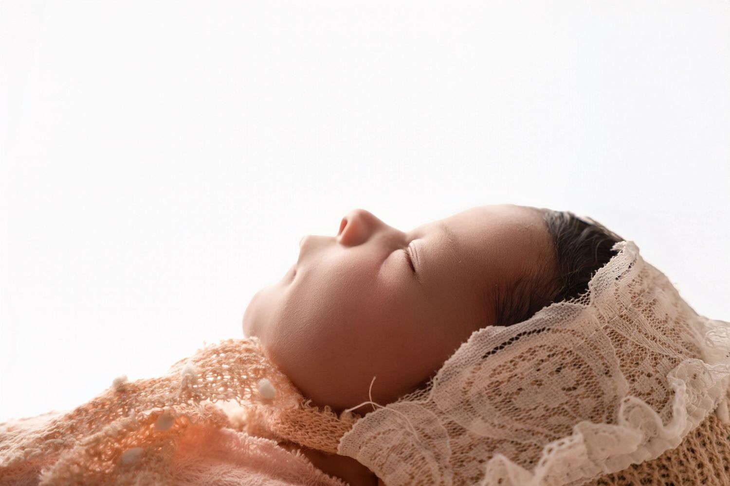 Peaceful newborn baby sleeping wrapped in lace and knit blanket against white background.