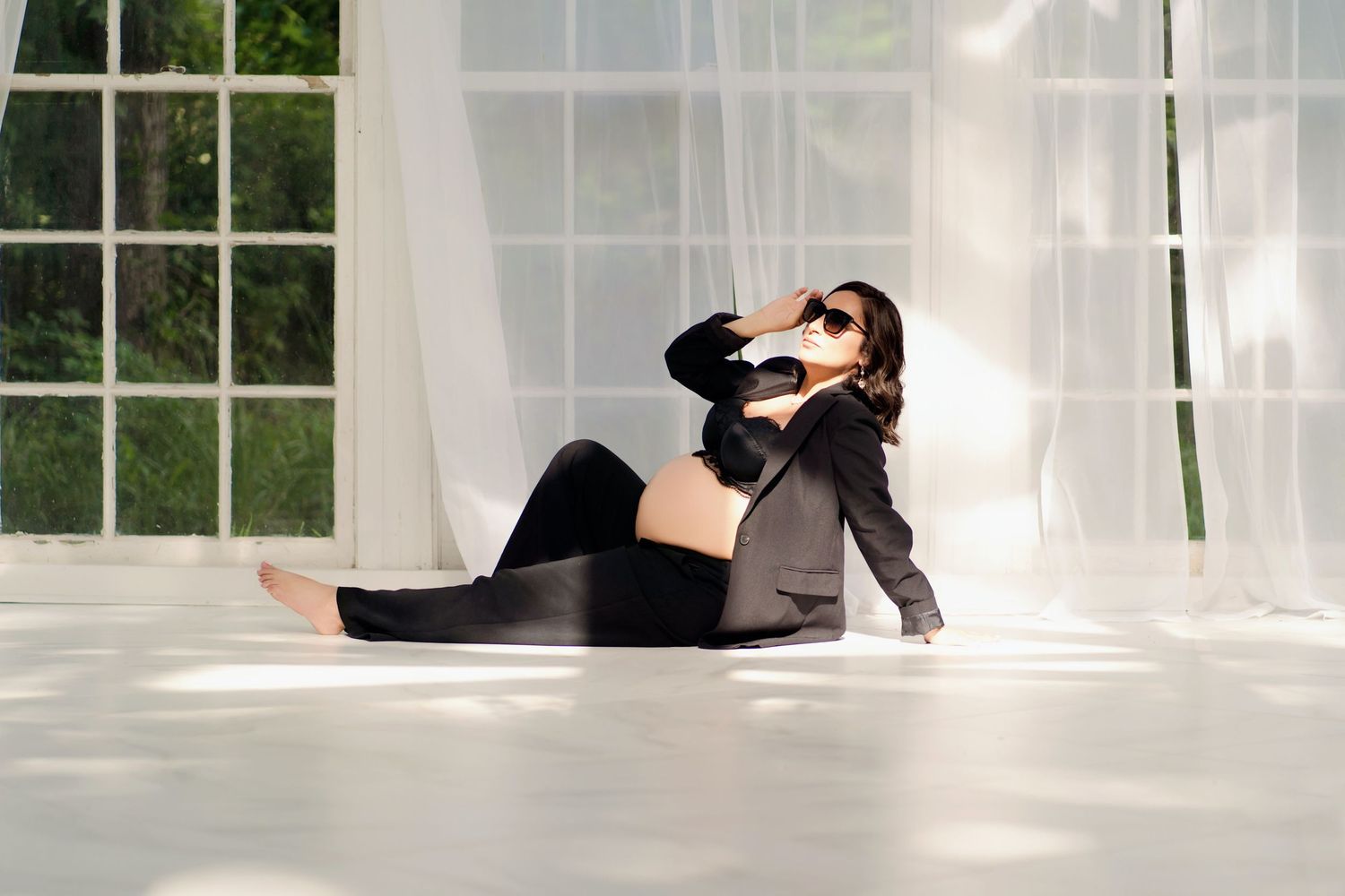A maternity session in a bright conservatory with white curtains and natural light.
