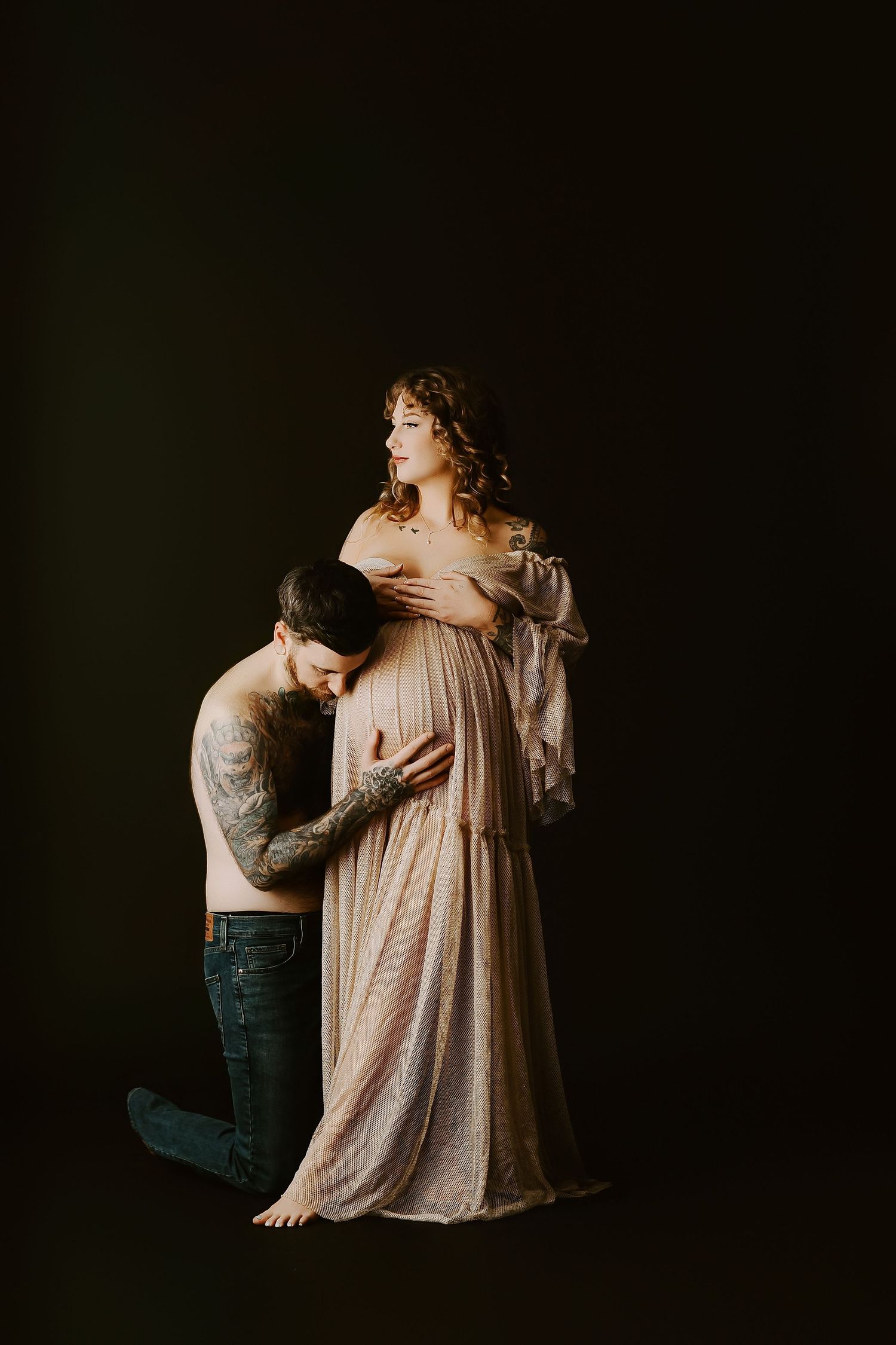 Intimate maternity portraits captured in dramatic low-key lighting against a dark background.