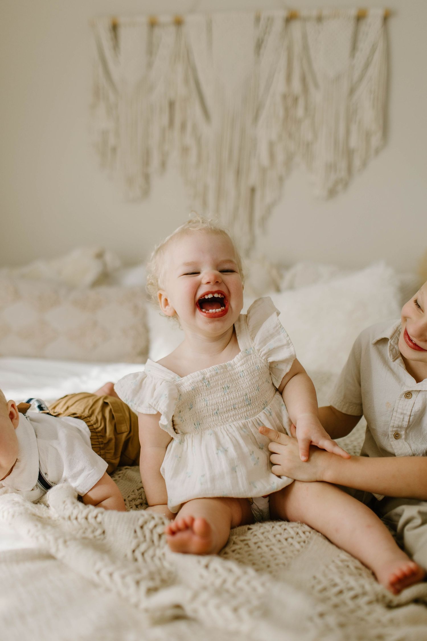 A baby laughs joyfully while lying on white bedding in a series of candid moments.