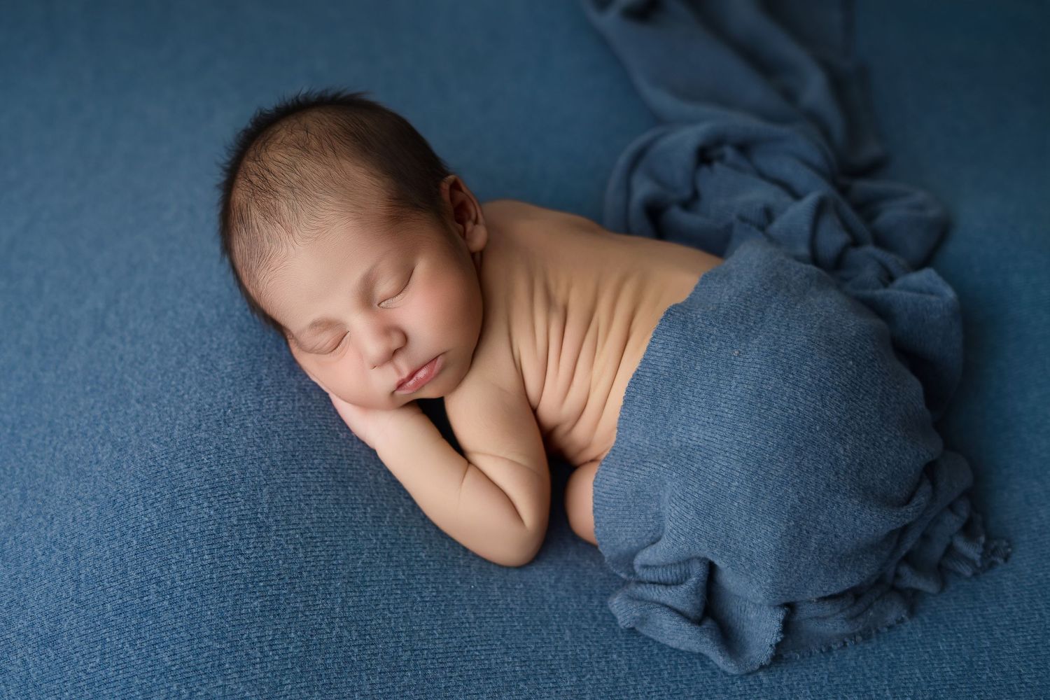 Newborn baby sleeping peacefully wrapped in a blue blanket on a soft blue background.