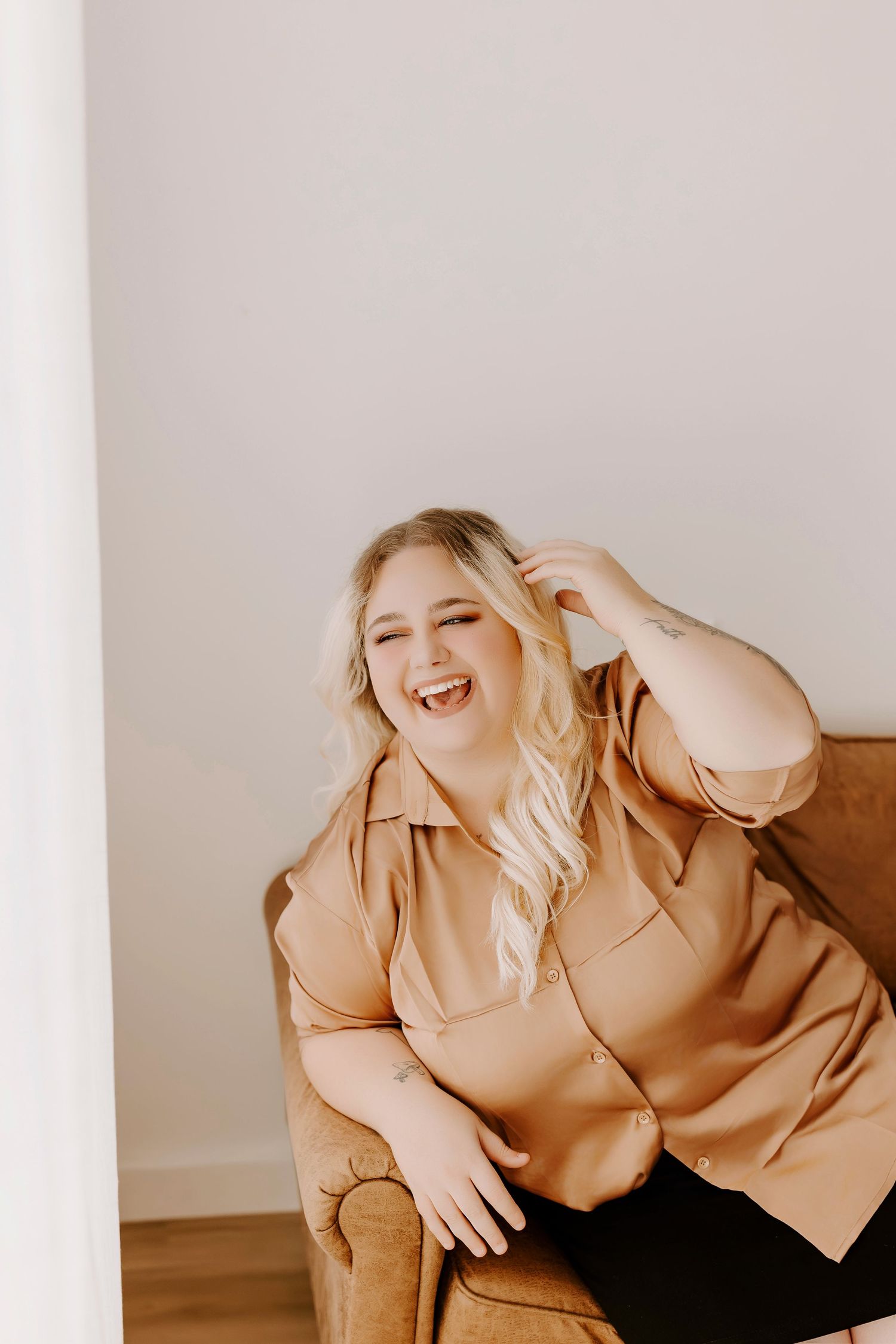 A person wearing a beige blazer leans back while laughing joyfully against a white backdrop.