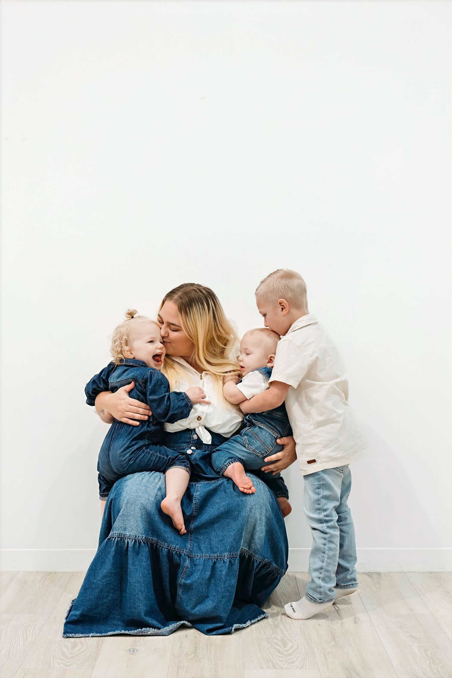 Family in matching denim outfits sharing tender moments on white floor during photo session.