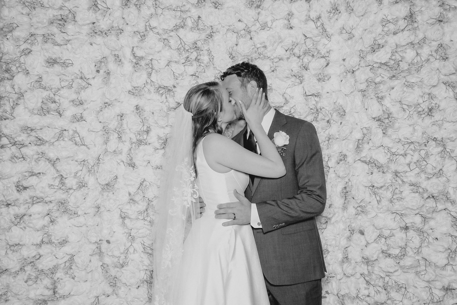 A romantic black and white wedding photo showing a couple sharing a tender moment against a textured floral backdrop.