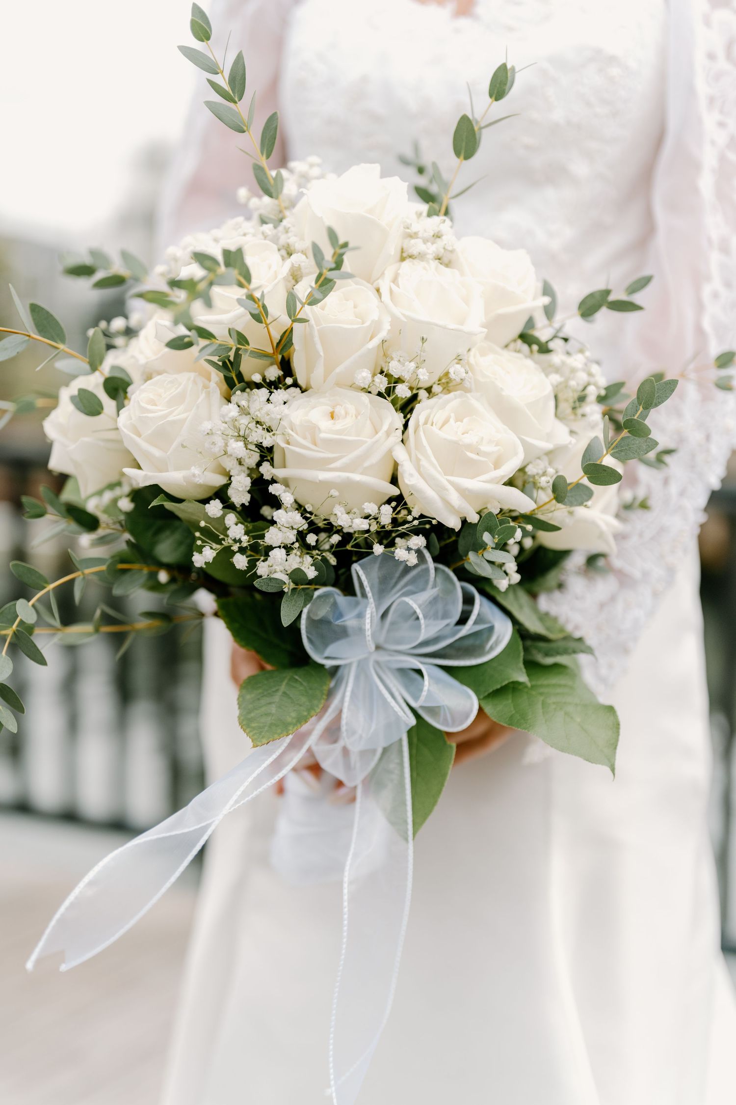 Elegant white rose wedding bouquet with delicate greenery and silver-blue accents.