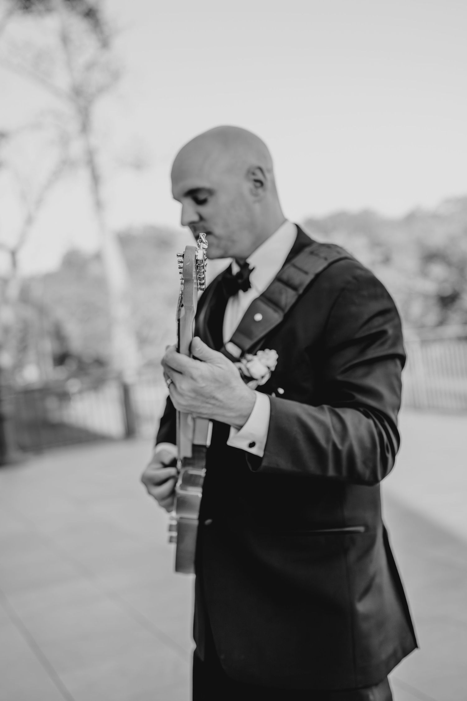 Black and white portrait of someone playing guitar outdoors while wearing a formal suit.