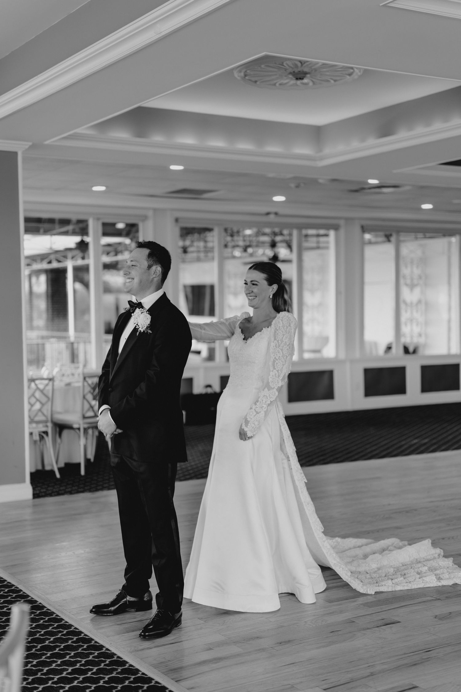 A bride and groom share their first look moment in a ballroom with hardwood floors and elegant decor.