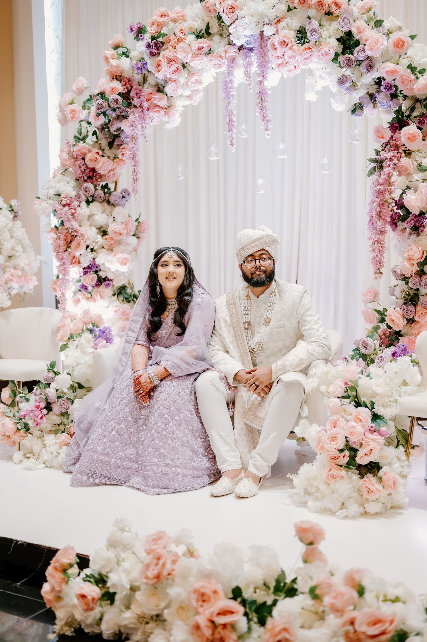 Elegant wedding setup with floral arches featuring pink and white roses, draped fabrics, and traditional decor.