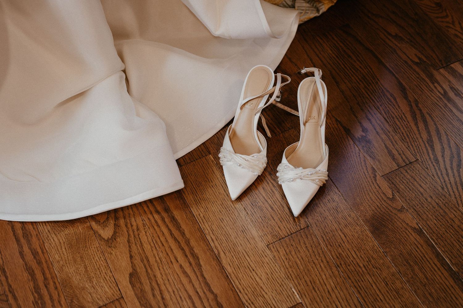 A delicate white lace wedding dress train flows across dark hardwood flooring in elegant detail.
