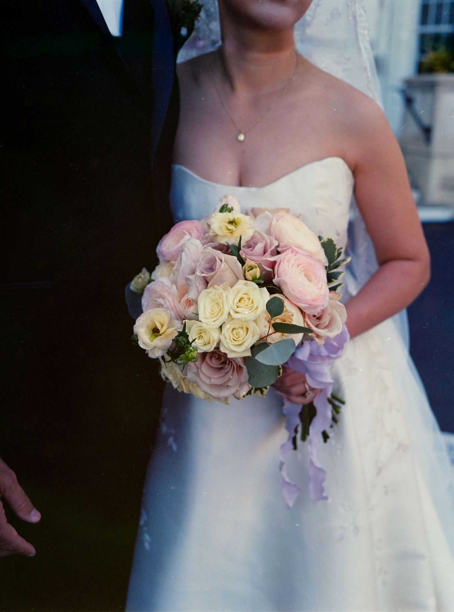 Delicate pink and white rose wedding bouquet held against a white bridal gown.
