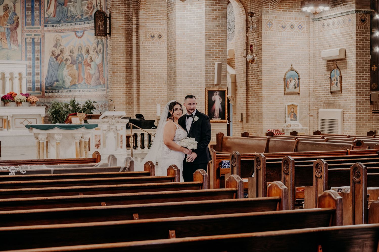 Wedding guests celebrate in a traditional church sanctuary decorated with ornate murals and wooden pews.
