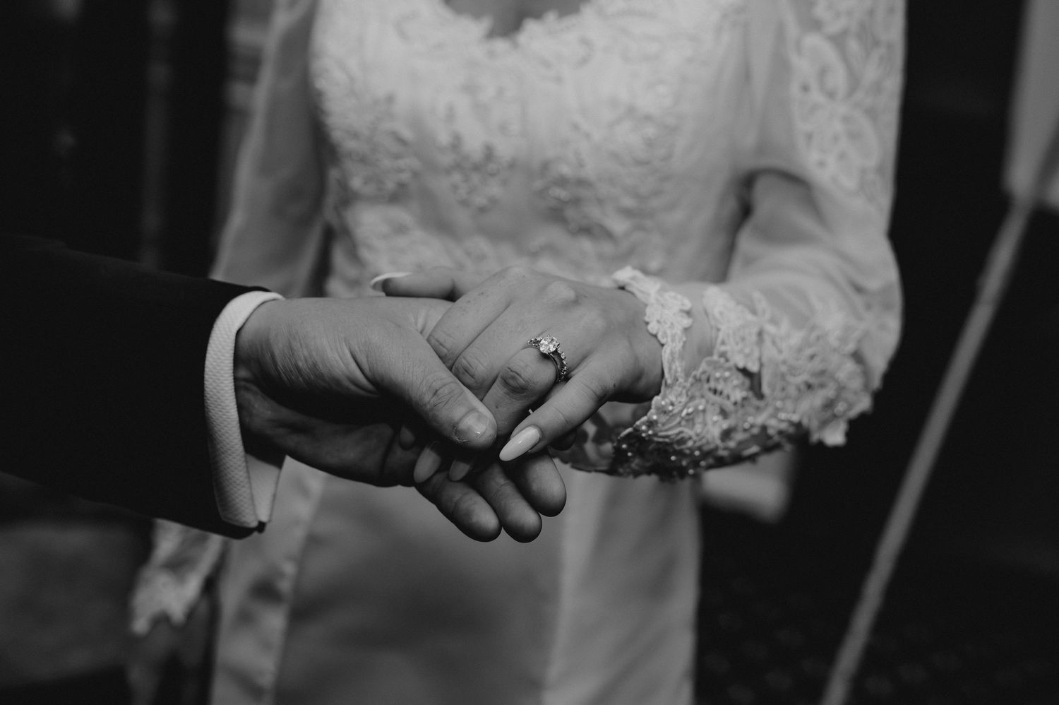 Black and white wedding photo showing hands holding a bouquet of flowers with a white lace dress in view.