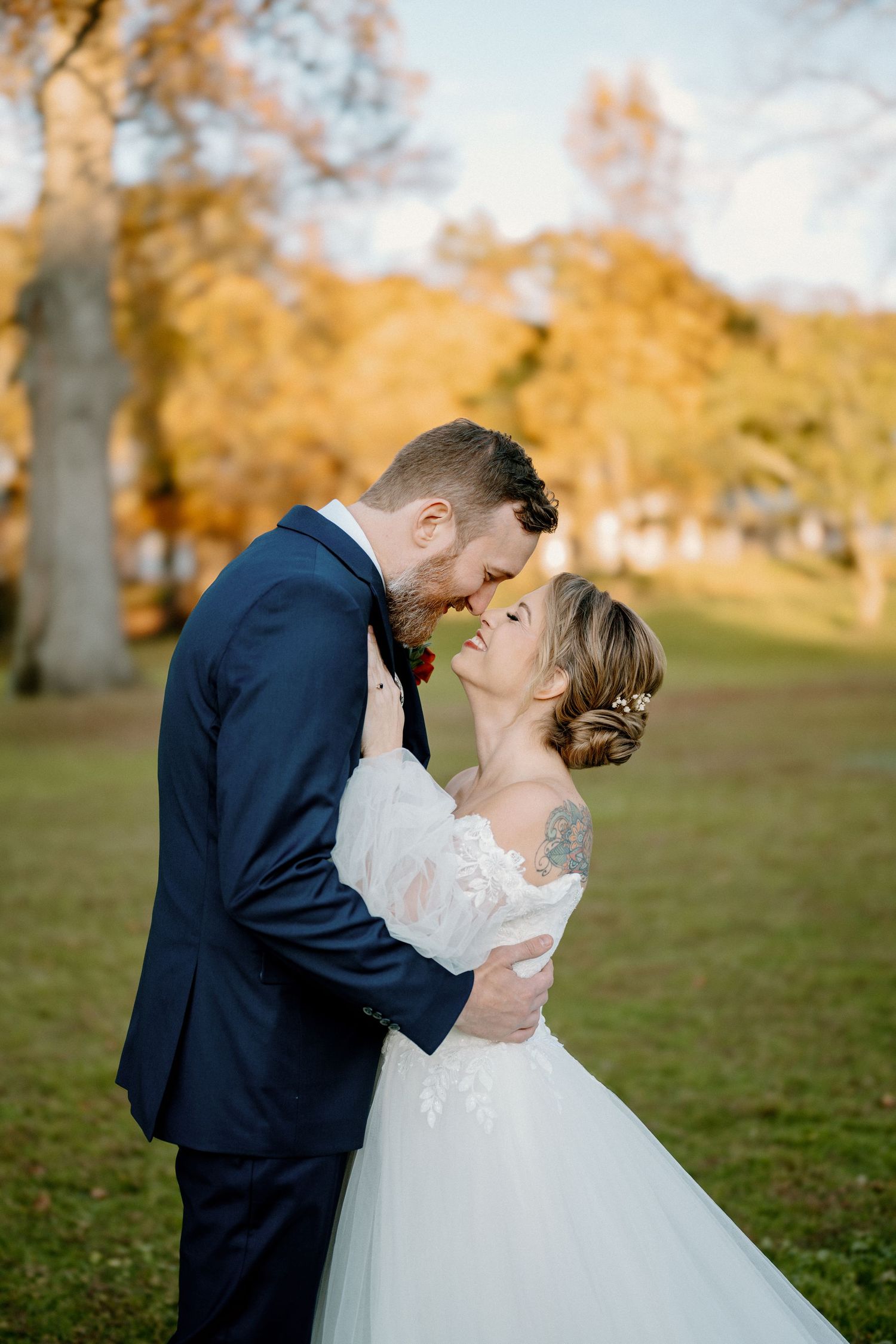 A bride and groom share a romantic moment outdoors in autumn, with golden foliage in the background.