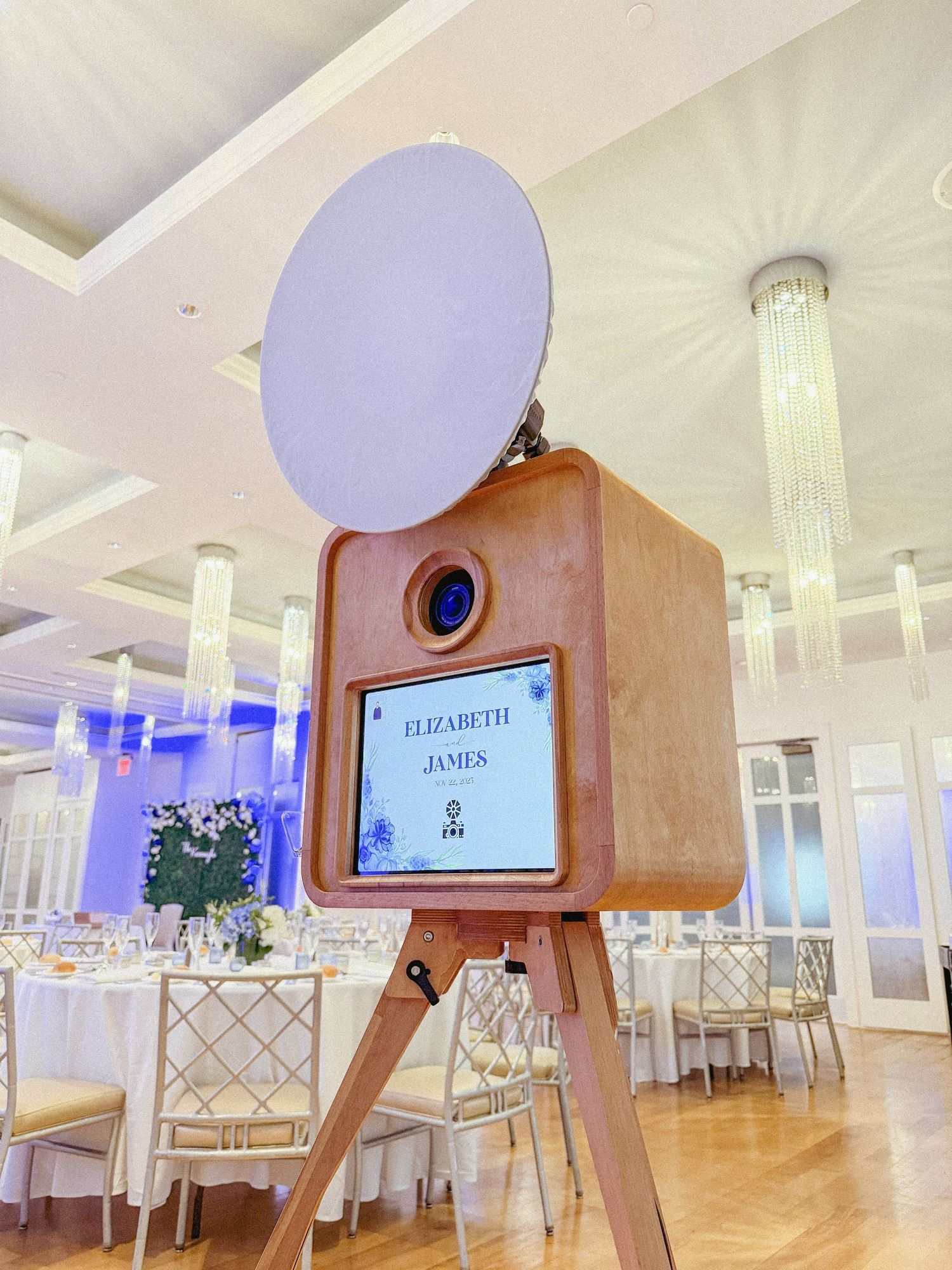 Modern photo booth display with wooden tripod stand and circular light in an elegant reception venue.