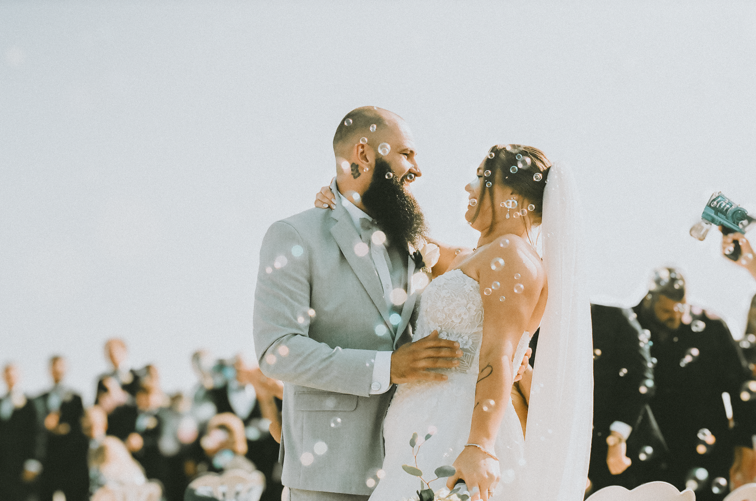 A couple shares a joyful moment during their outdoor wedding ceremony as guests look on in the background.