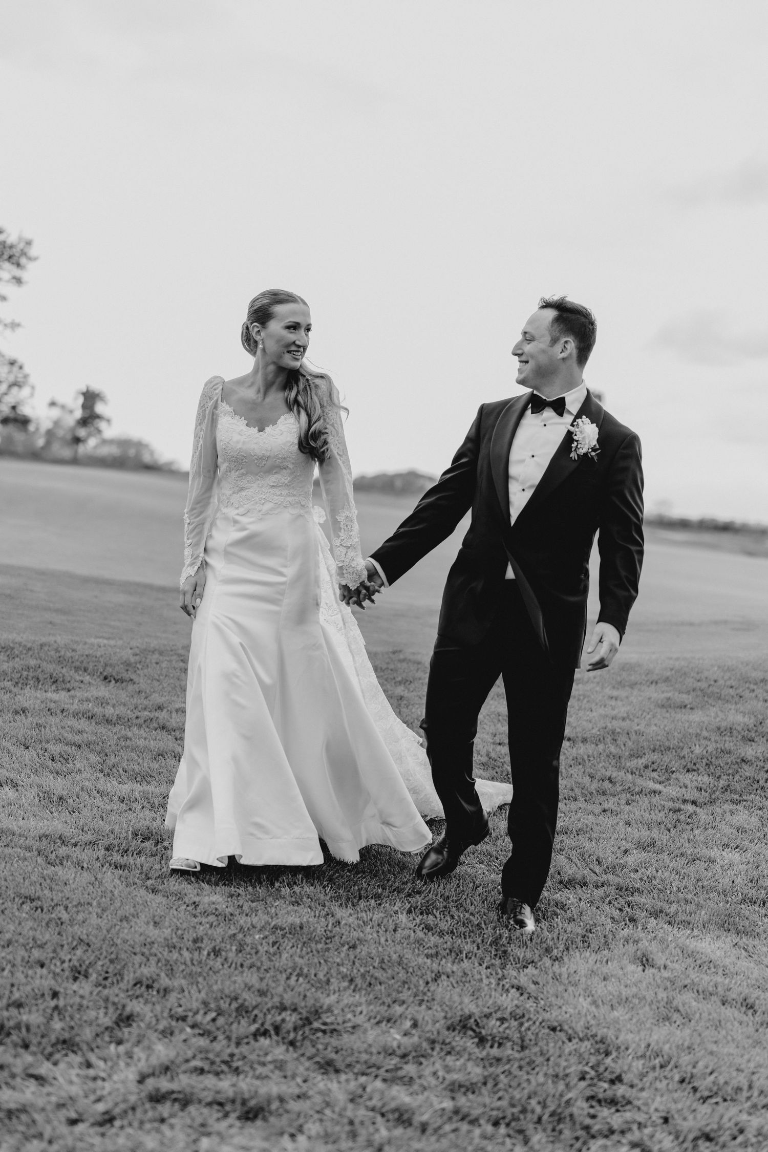 Black and white photos of a couple walking together on grassy hill.
