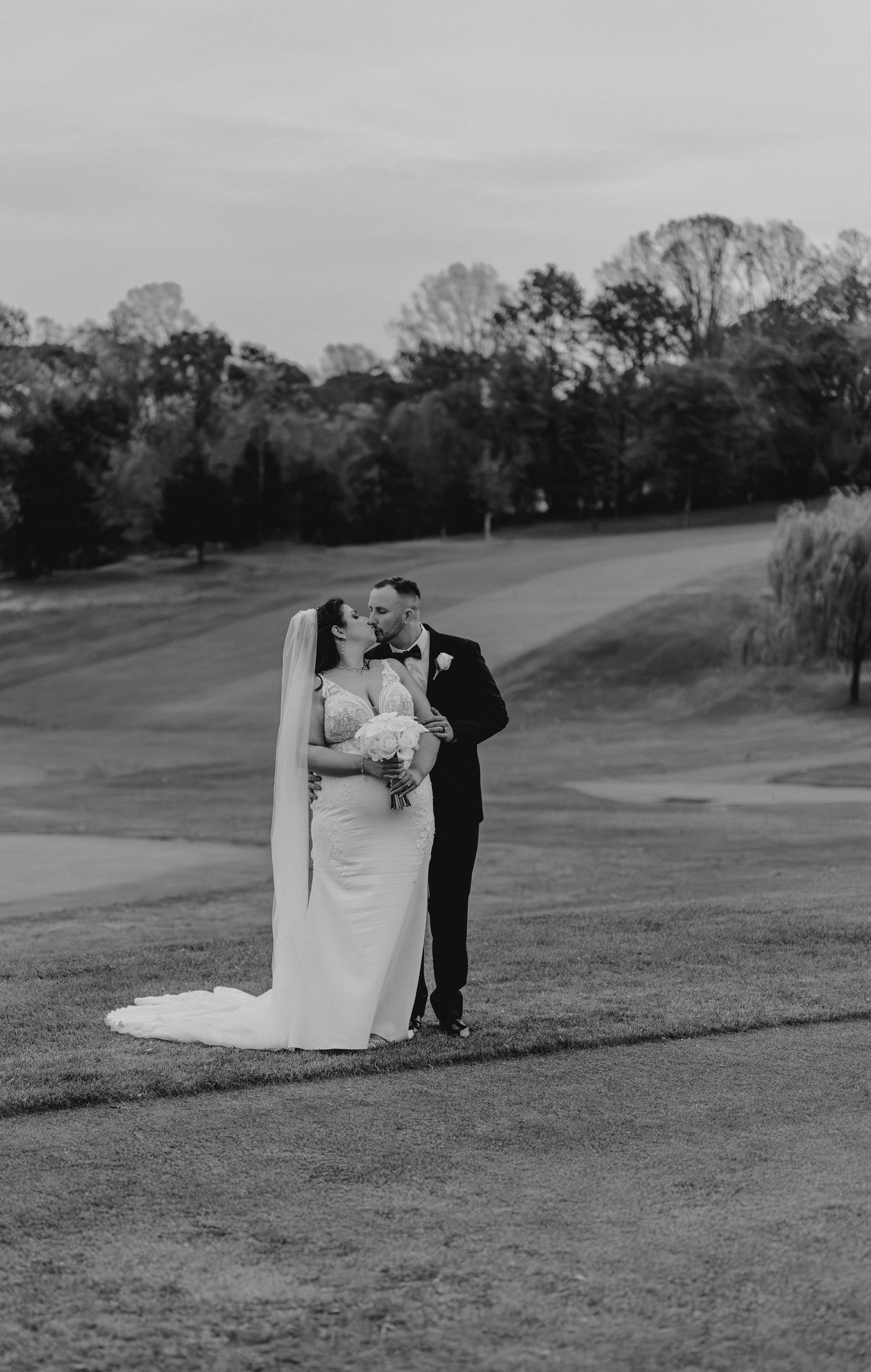 A couple shares a romantic moment in black and white on a rolling golf course landscape.
