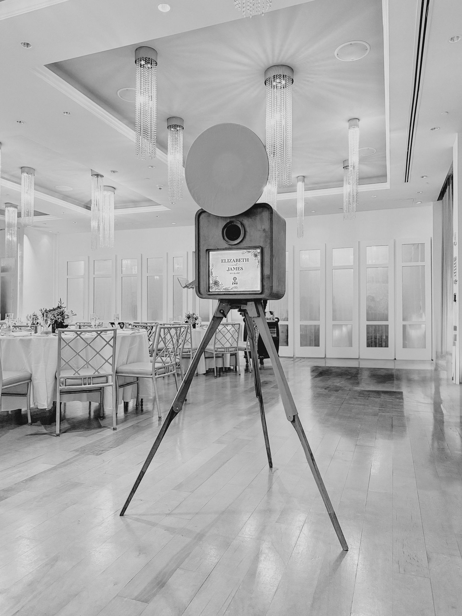 Vintage photo booth camera setup in an elegant ballroom with crystal chandeliers and dining tables.