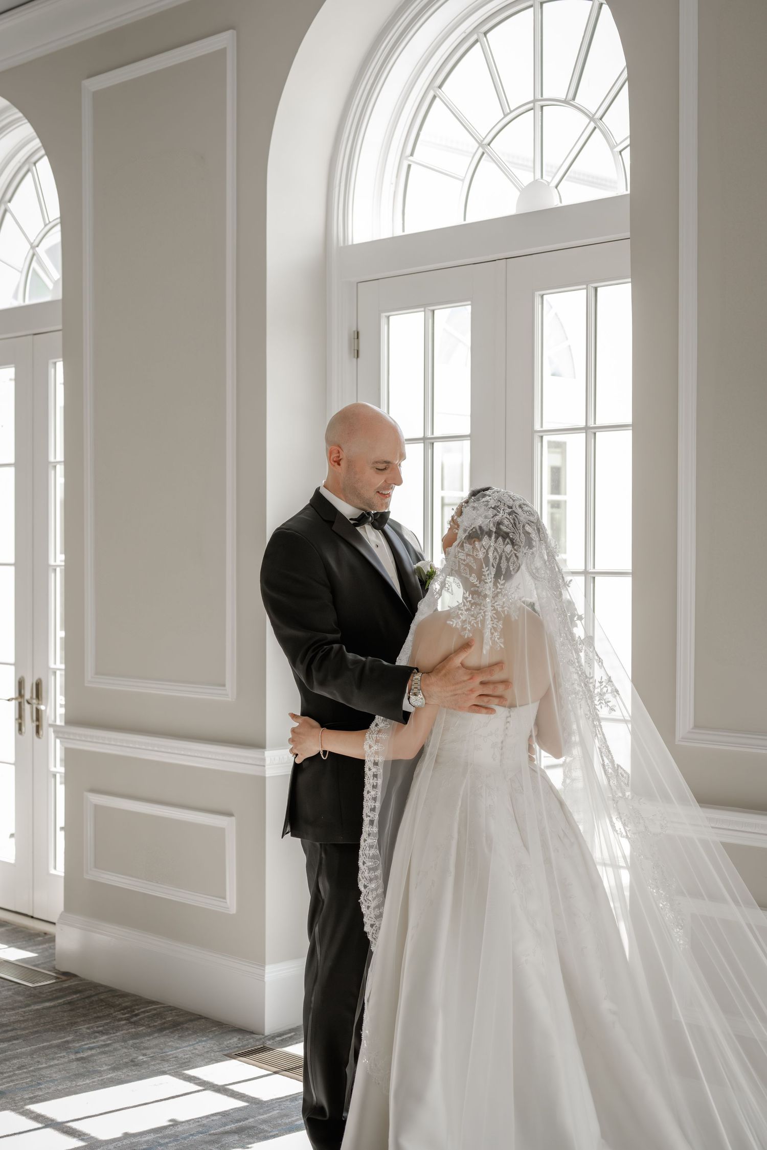 Elegant white room with arched windows and couple sharing first look moment.