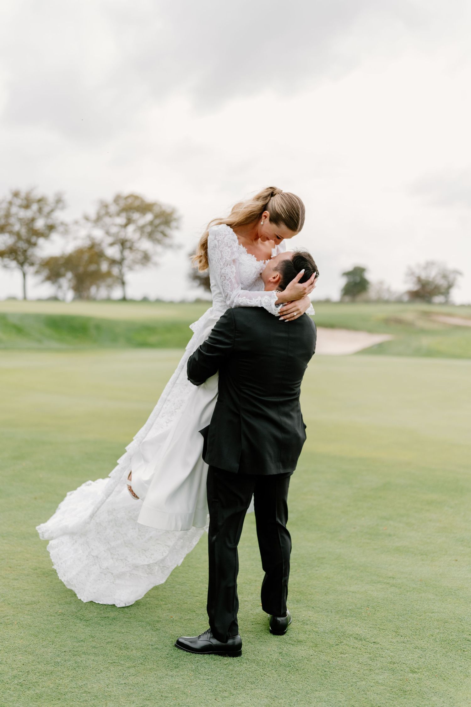 A romantic wedding couple dips and embraces on a lush green golf course during their photo session.