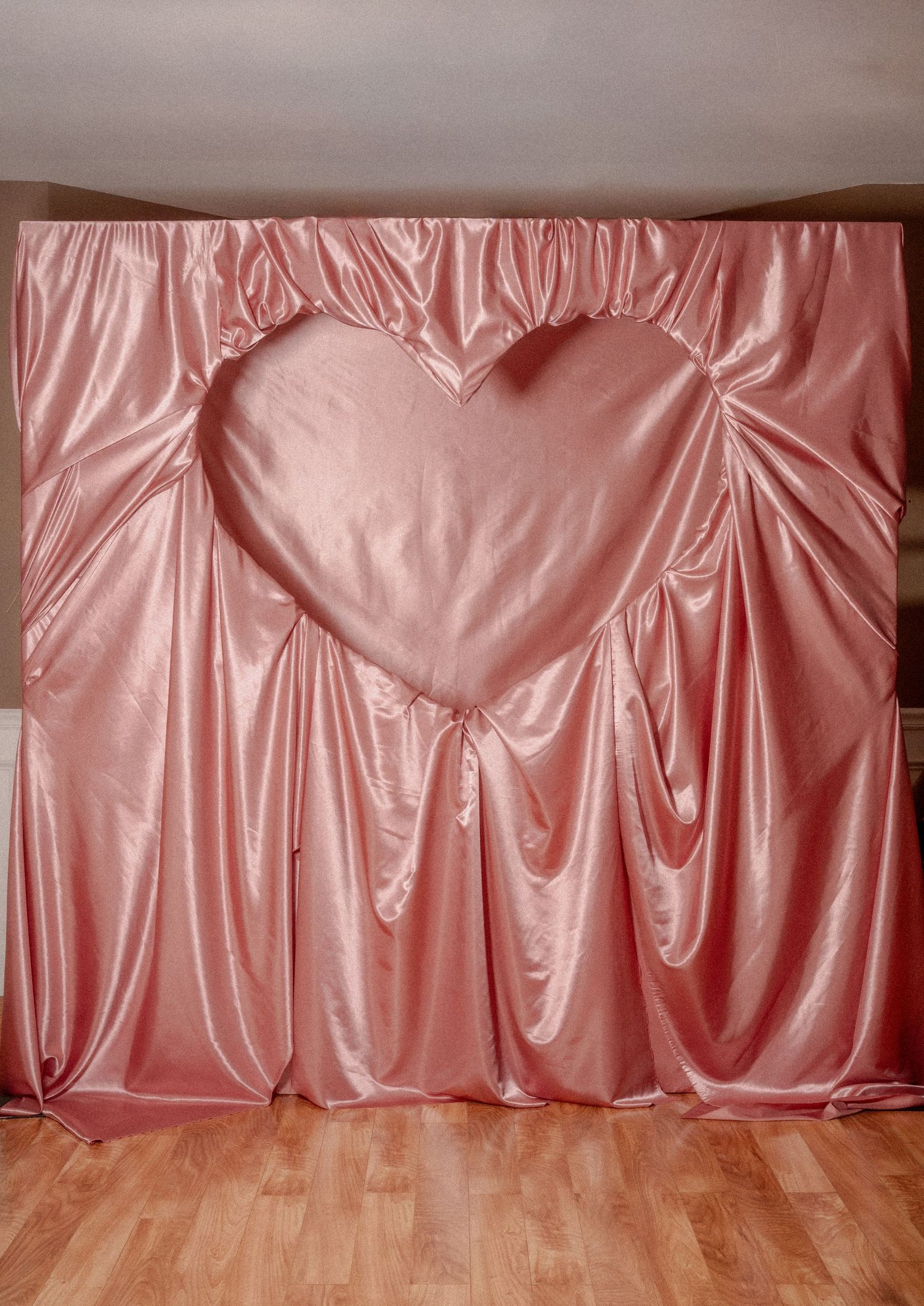 Pink satin fabric backdrop with a large heart-shaped design in the center creating an elegant romantic setting.