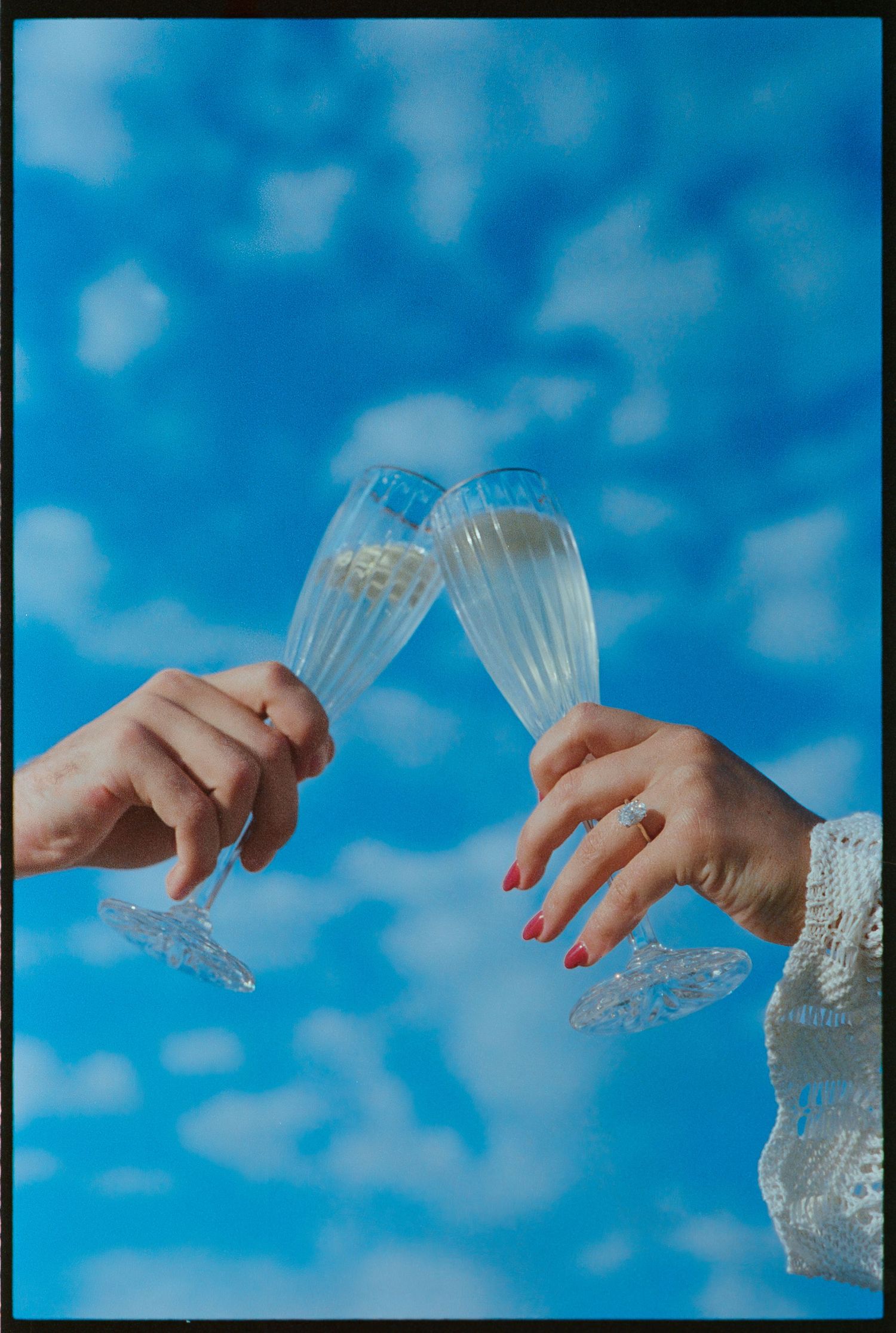 Hands holding bubble wrap against blue cloudy sky background.