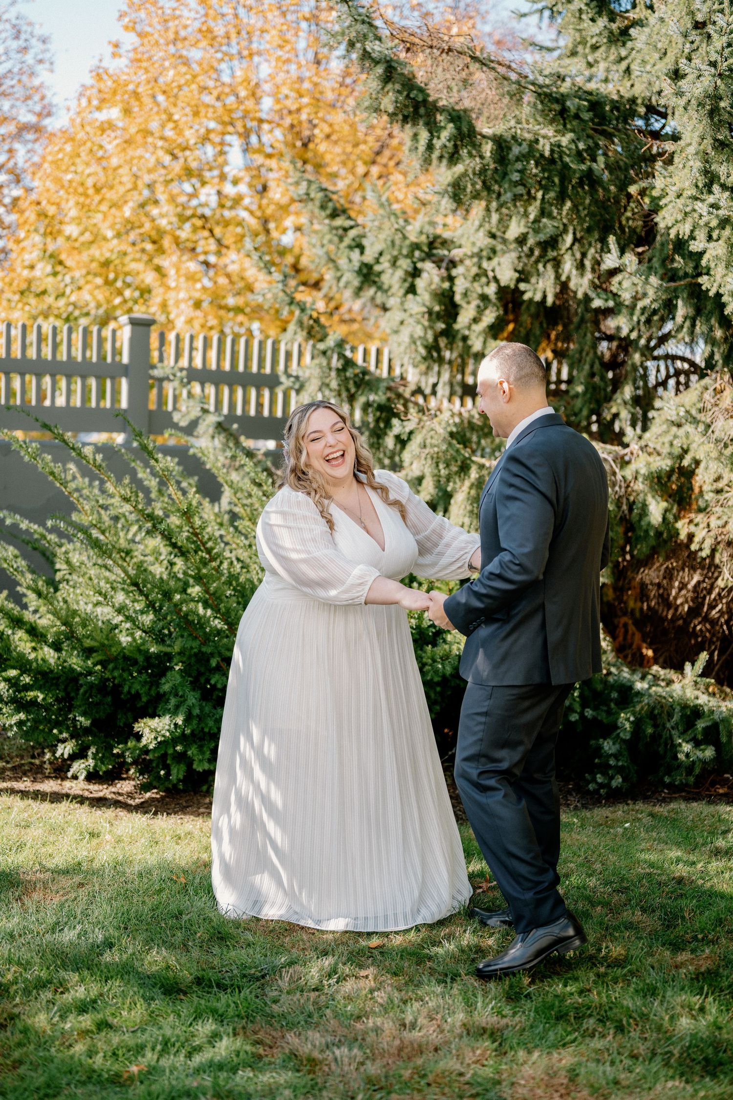 A couple shares a playful moment outdoors during a fall wedding photoshoot with autumn foliage in the background.