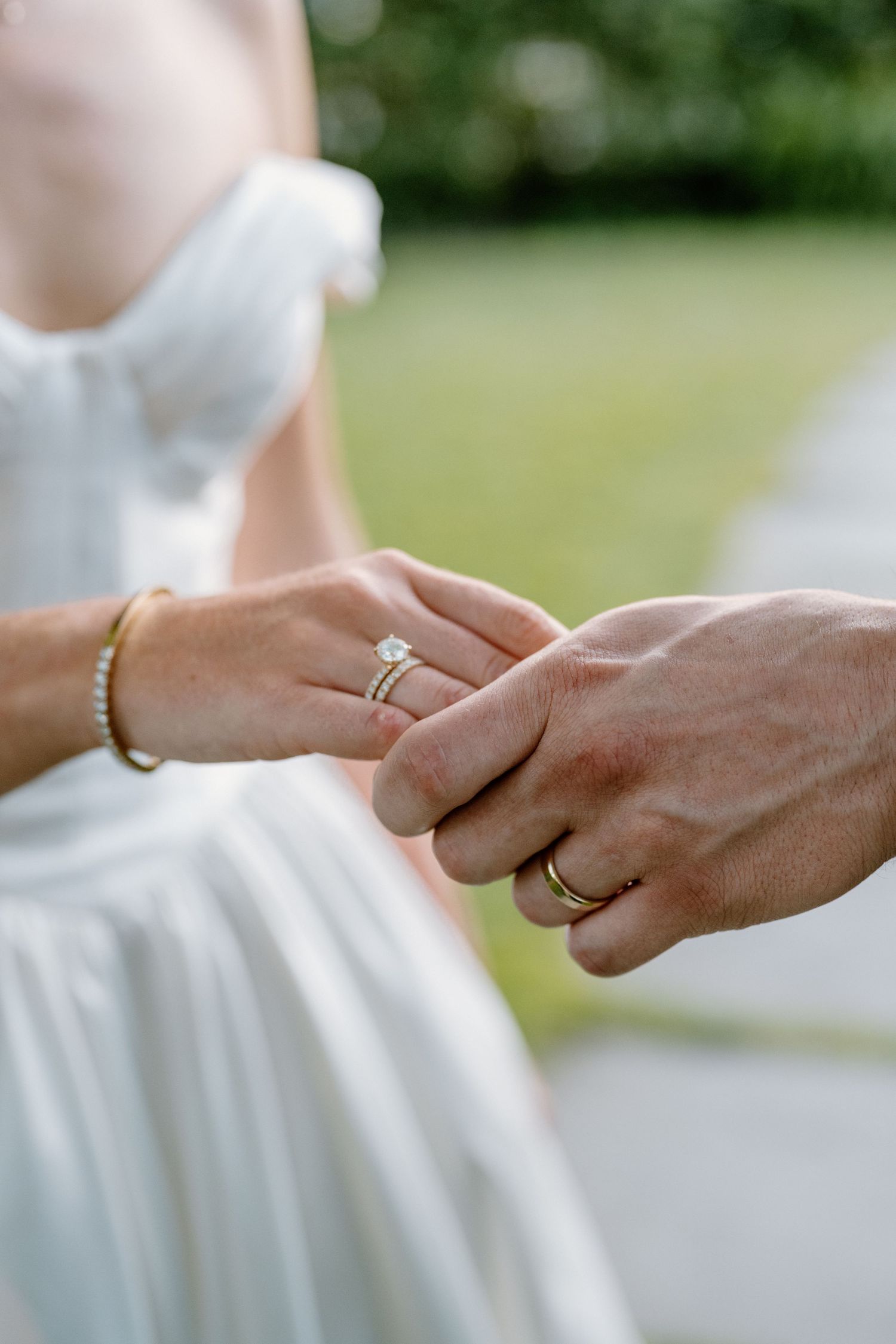 Bride and groom holding hands, showcasing diamond engagement ring and gold wedding band on their wedding day.