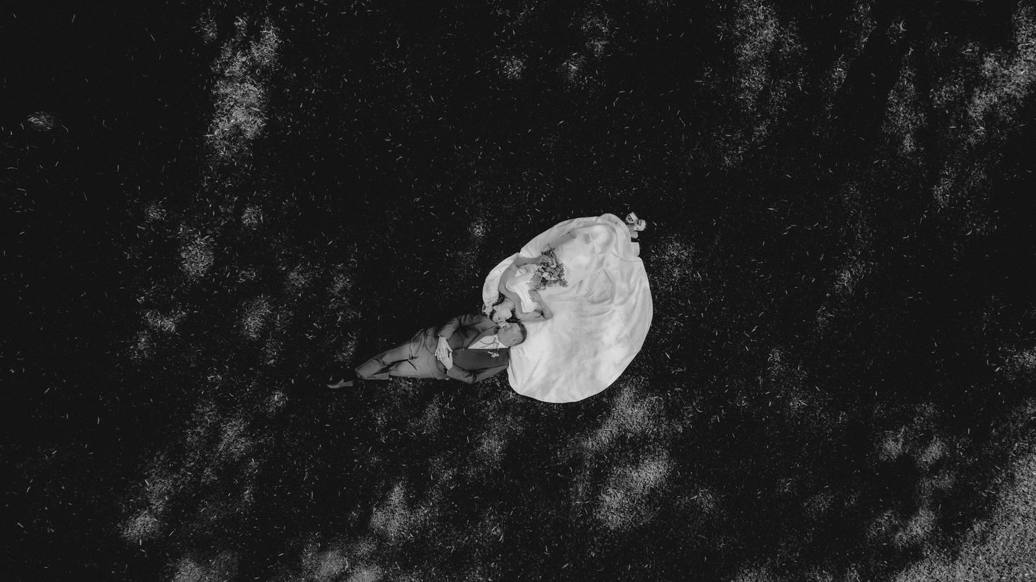 Aerial black and white photo of a person lying on dark ground beside a white fabric or parachute.