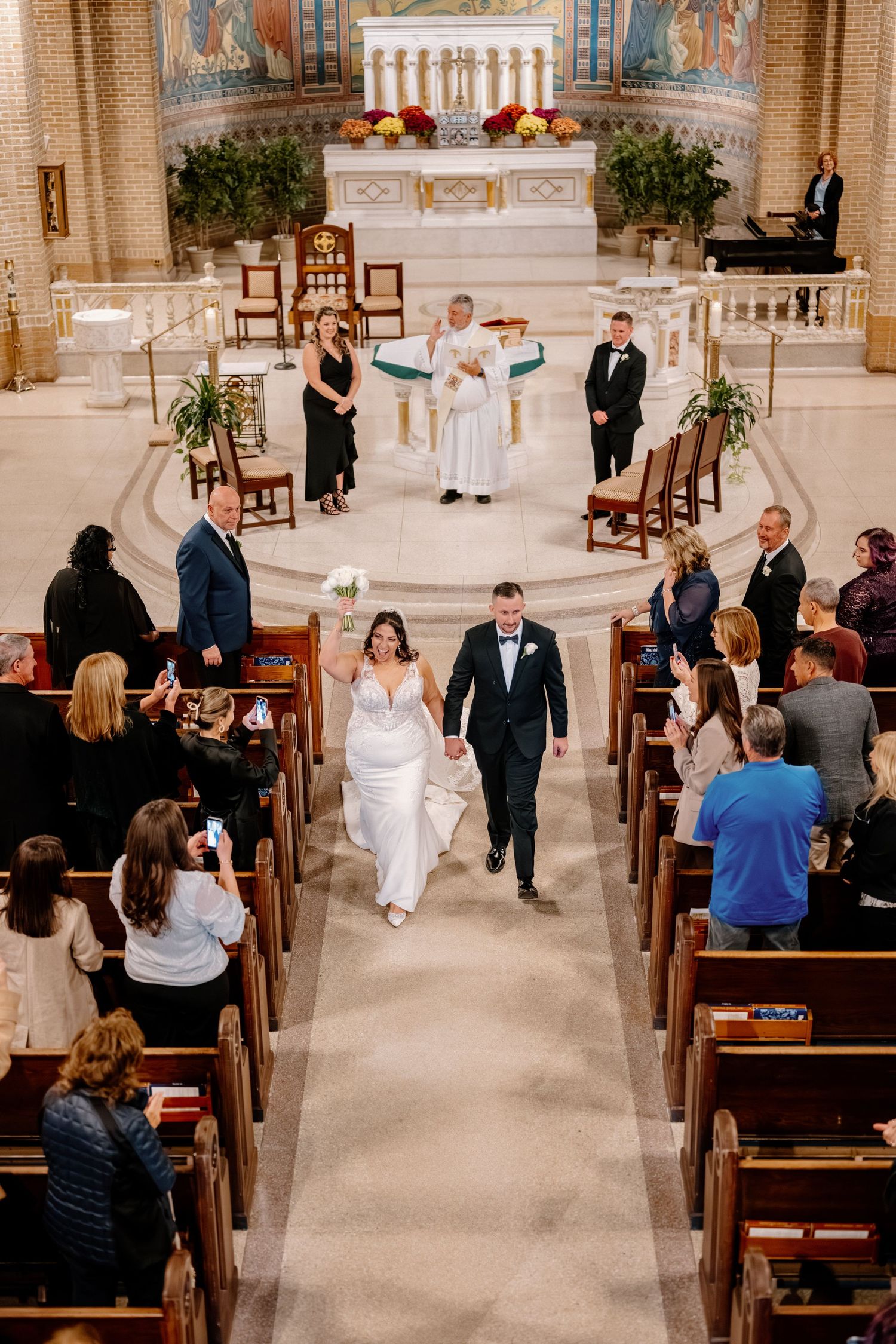 Wedding ceremony in progress inside an ornate church with guests seated in wooden pews.