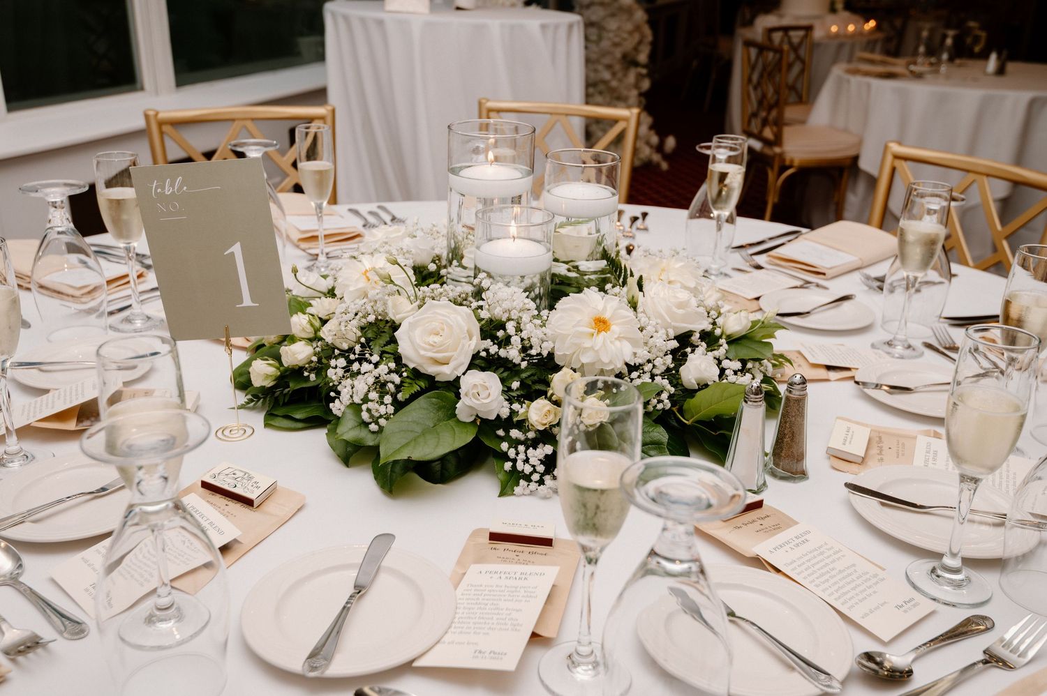 Elegant wedding reception tables set with white linens, floral centerpieces and cross-back chairs.