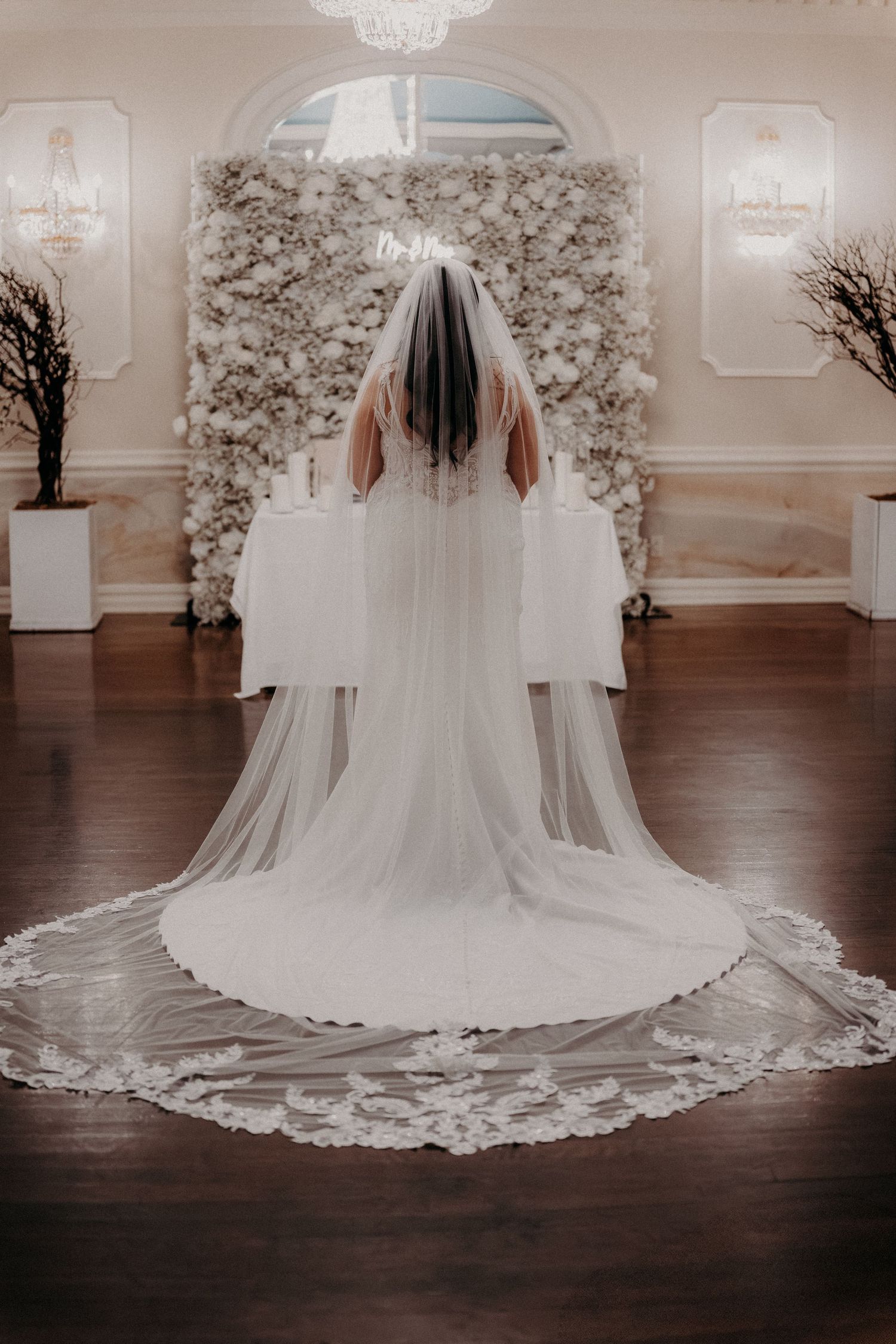 A stunning cathedral-length wedding veil with intricate lace details spreads across dark hardwood floors in an elegant room.