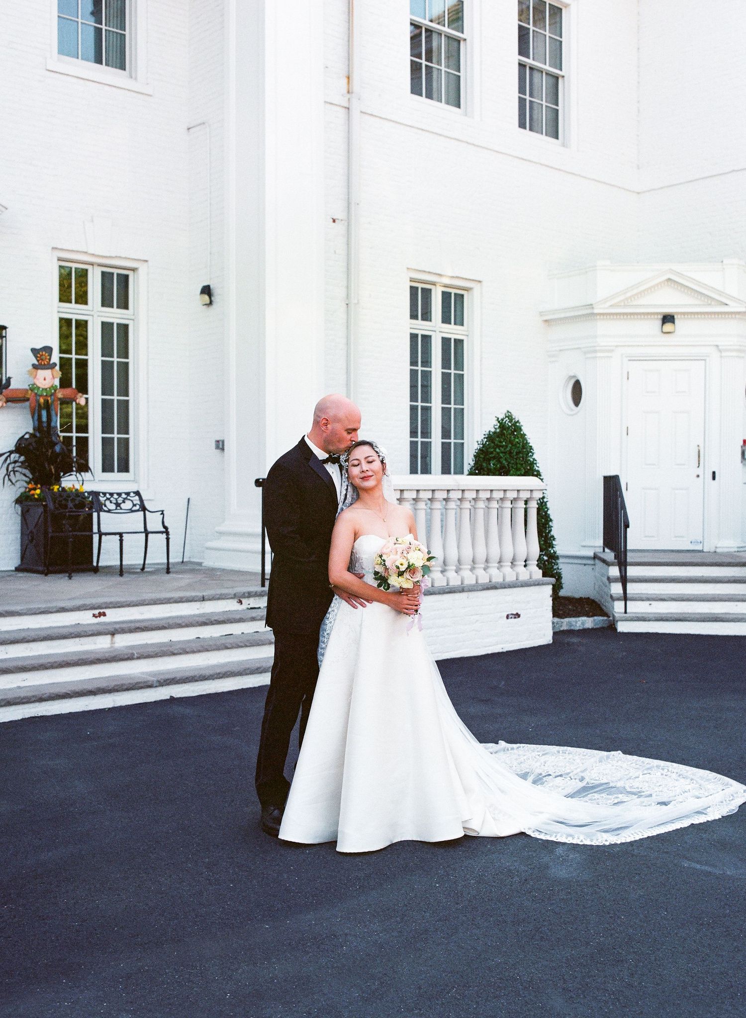 Wedding couple posing on black pavement in front of grand white building.