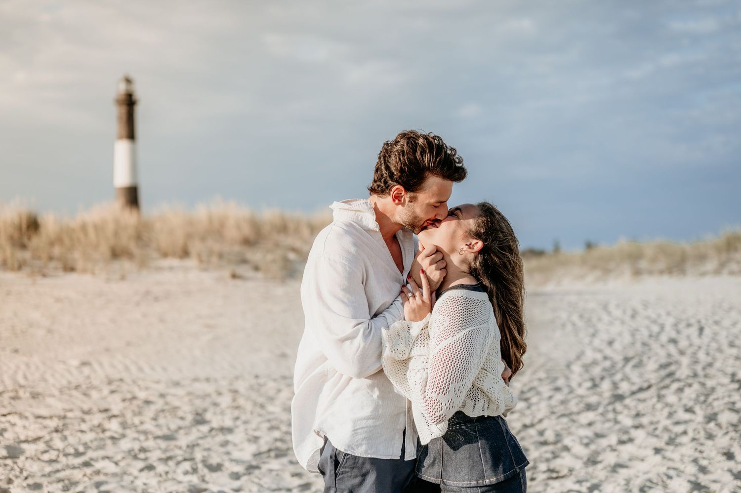 A romantic moment on the beach with a lighthouse in the background.